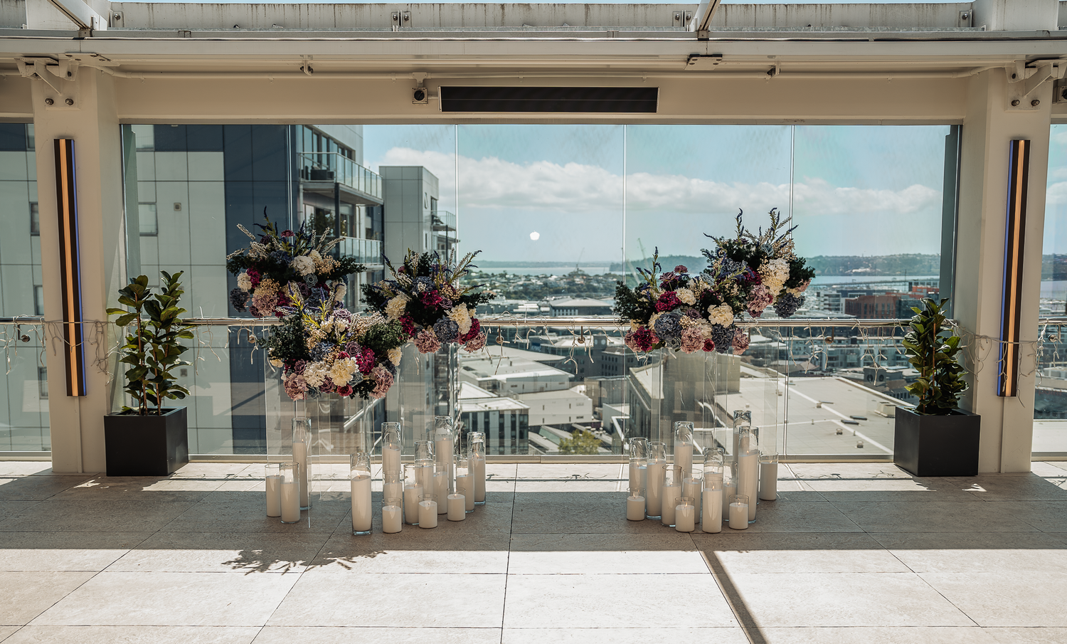 Modern wedding ceremony setup with floral arrangements and candles overlooking city view.