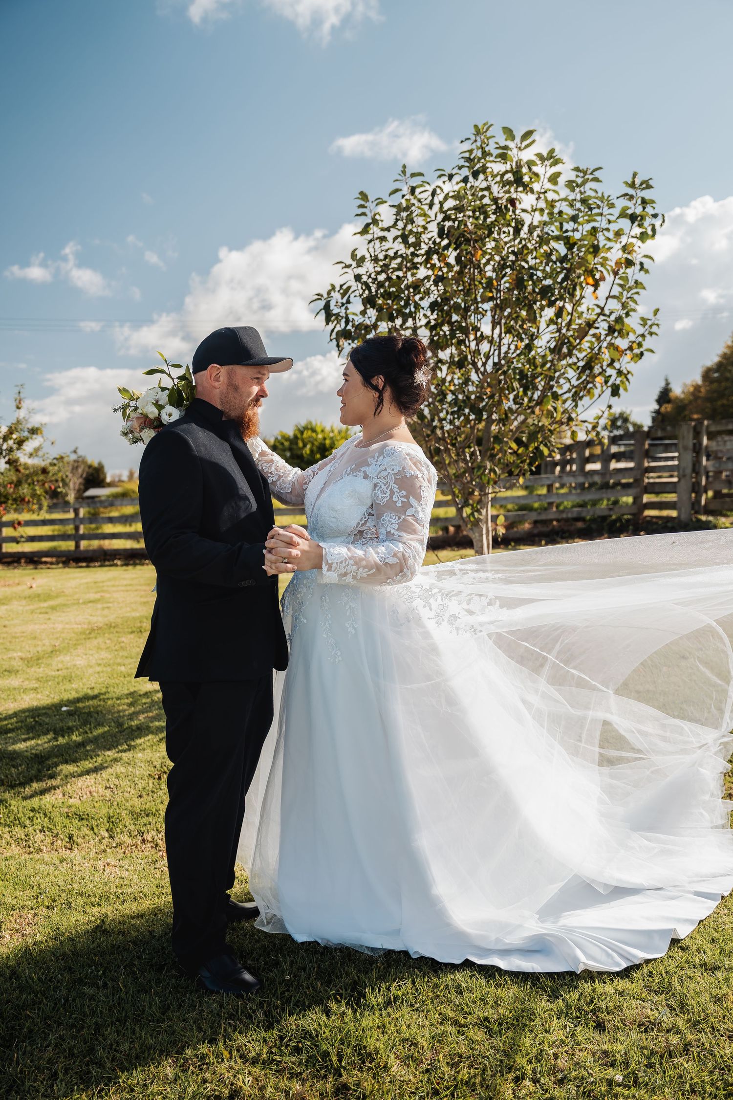 A wedding couple shares an intimate moment in a sunny garden setting with a long flowing veil.