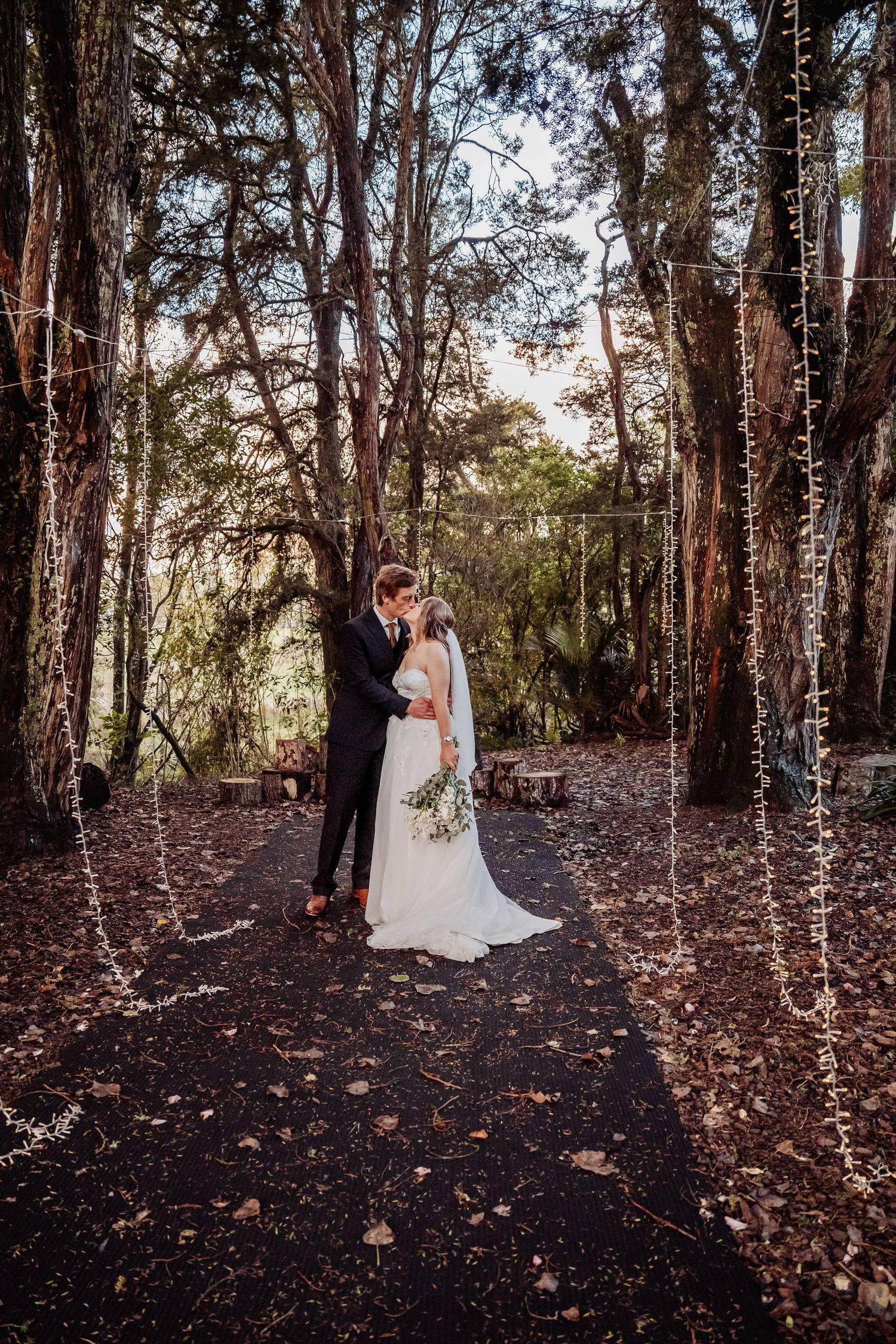 A romantic woodland wedding scene with string lights illuminating a forest clearing at dusk.