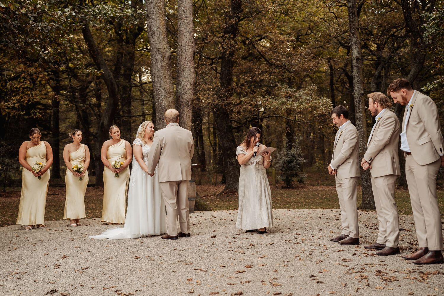 Wedding ceremony in autumn forest with bridesmaids in yellow dresses and groomsmen in tan suits.