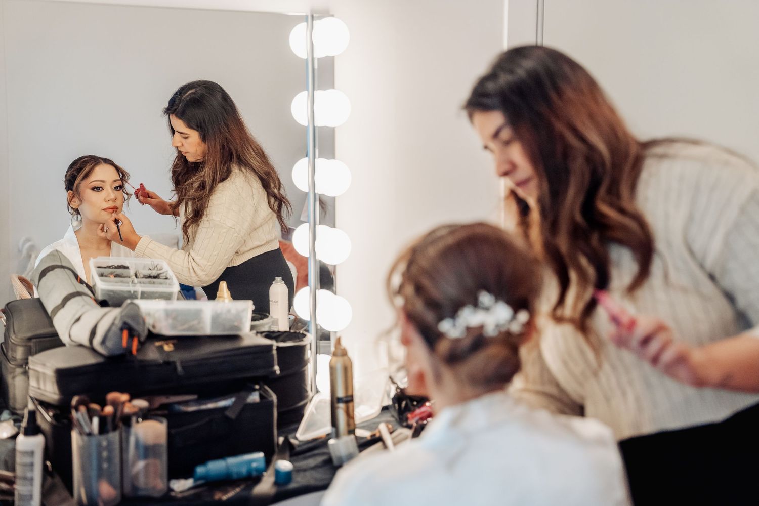 Professional makeup artist applying cosmetics at a beauty salon with vanity lights and mirror setup.