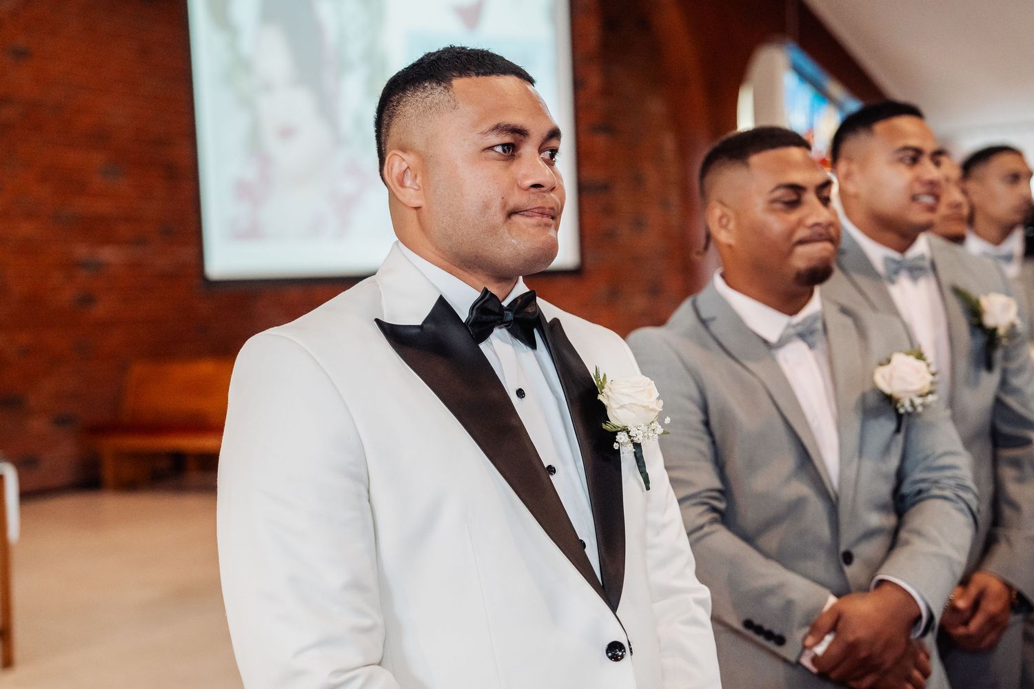 Wedding party members in light gray suits seated during formal ceremony.
