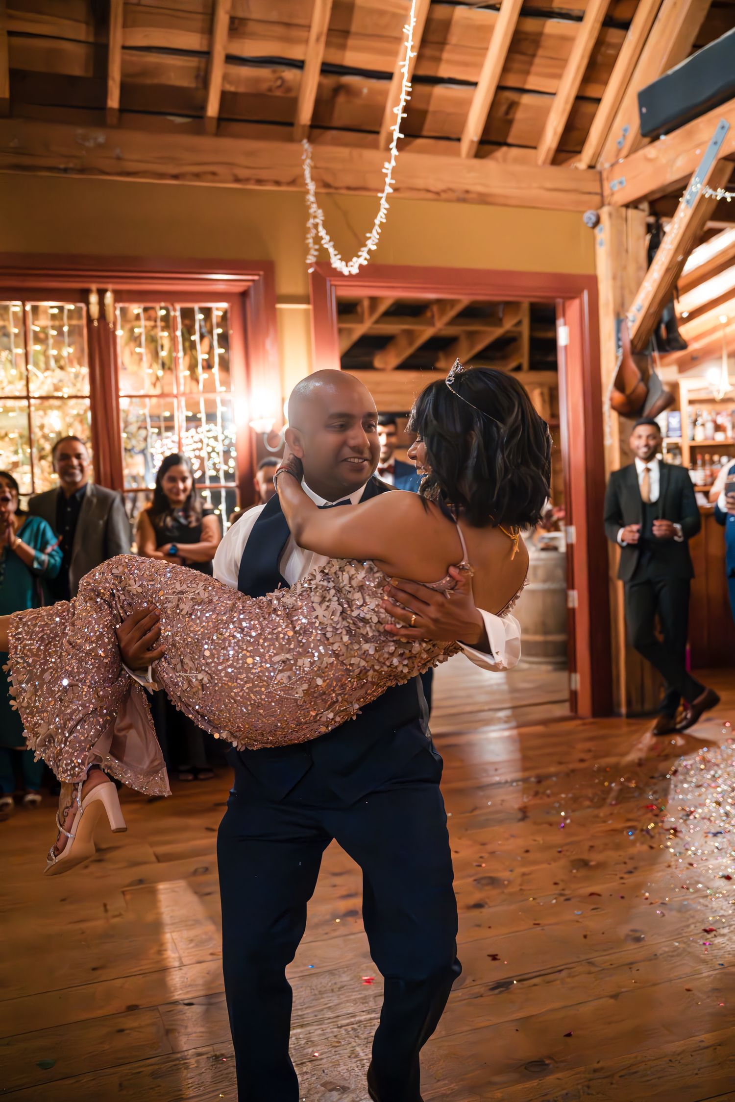 A groom carries his bride in a sparkling dress during their wedding dance.