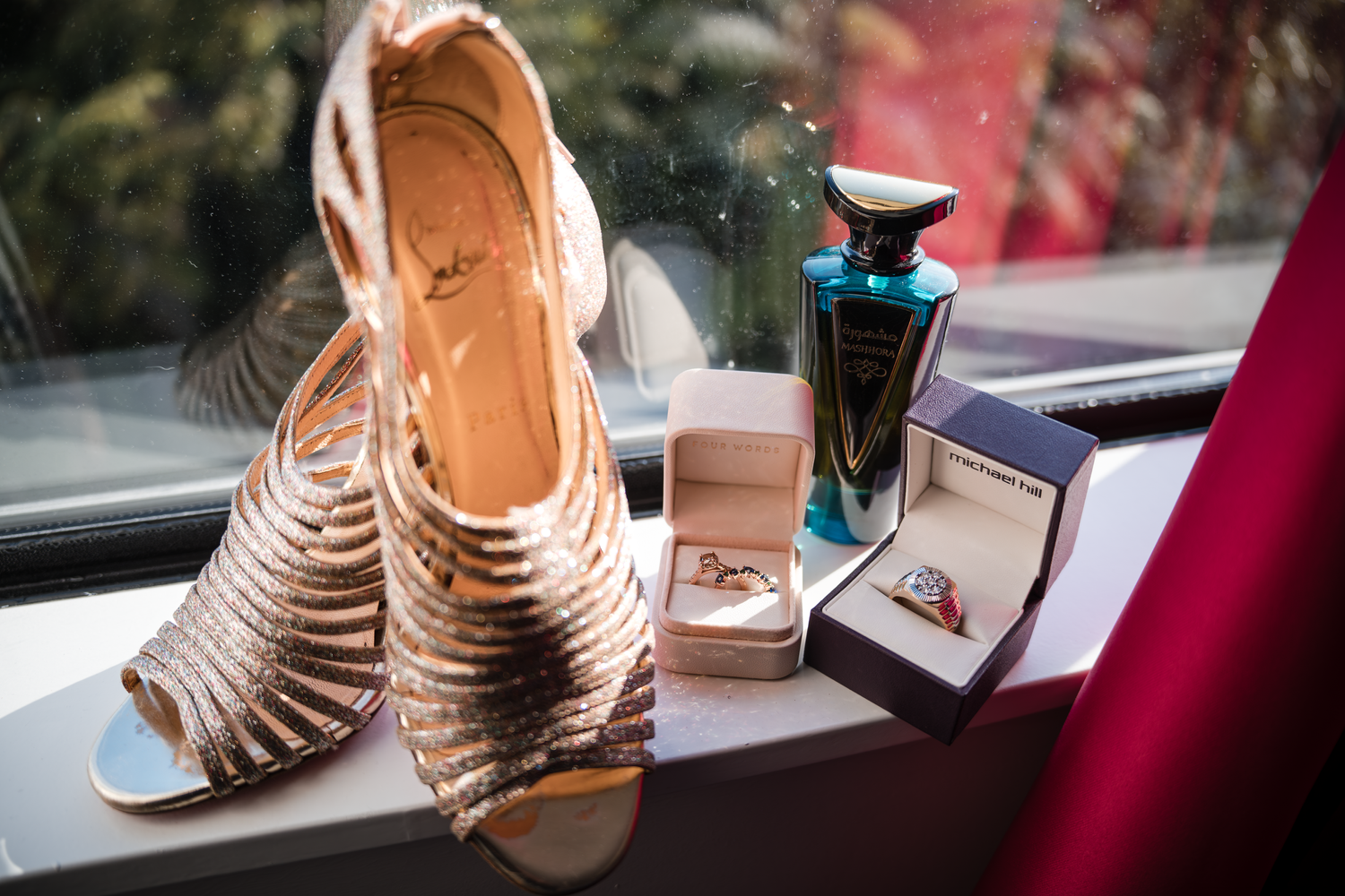 Wedding accessories including strappy heels, perfume, and jewelry displayed on a windowsill.
