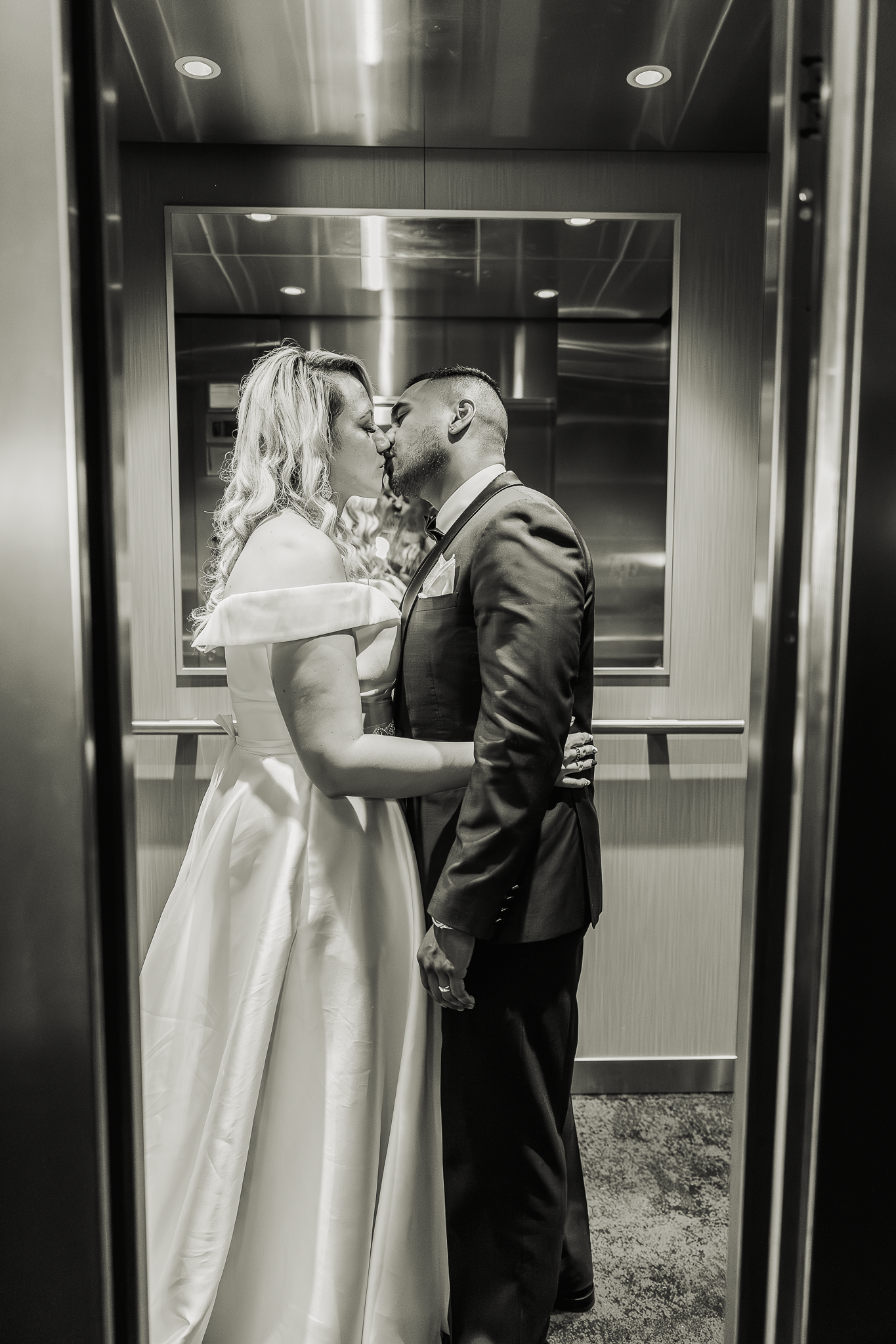 Intimate black and white elevator portrait of newlyweds sharing tender moment.