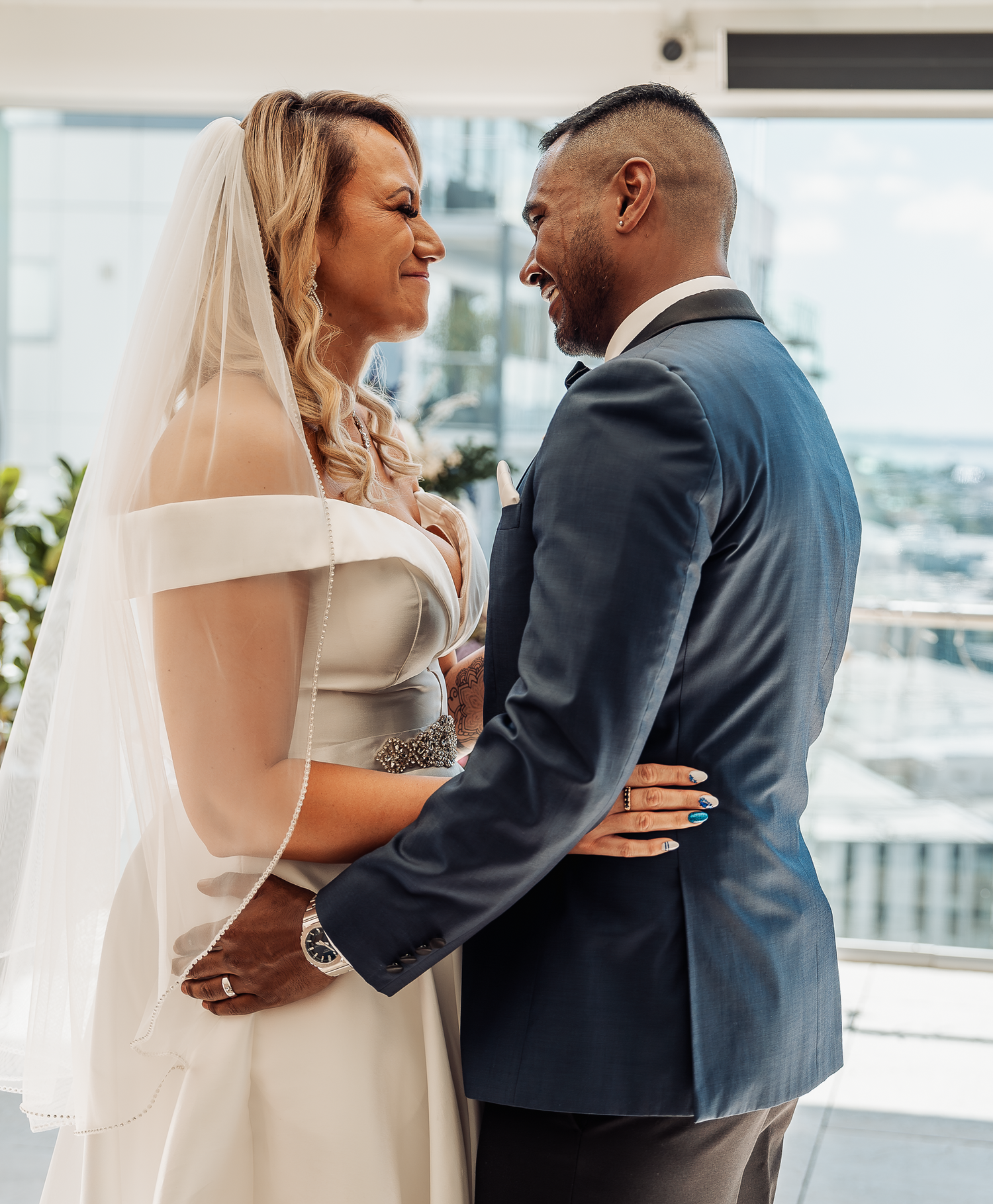 The bride and groom share a loving moment by large windows overlooking the city.