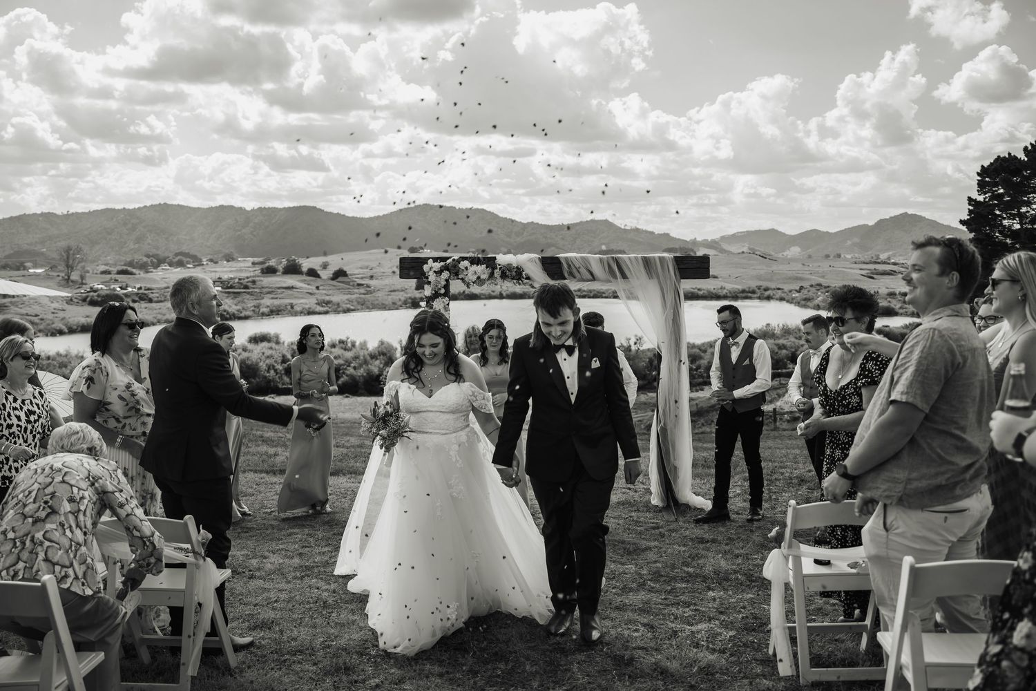 Bride and groom walking back down the aisle as guests toss confetti at an outdoor wedding ceremony.