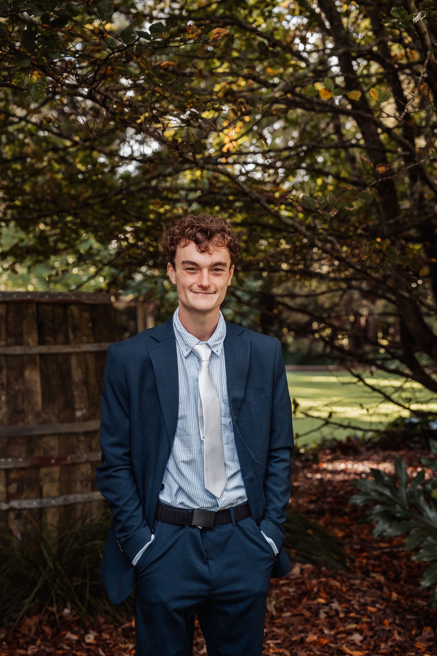 Young groom in navy suit smiling in autumn garden.