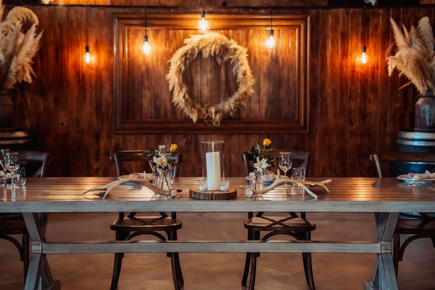 Rustic wedding reception table set with elegant place settings, candles, and wildflowers in a warm wooden venue.