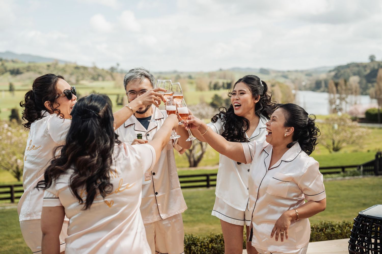Bridesmaids in white dresses laughing and having fun during a photo session in a scenic outdoor setting.