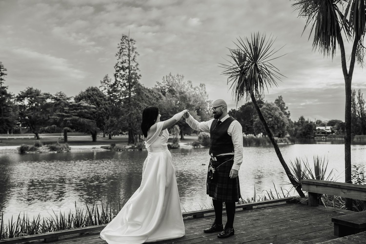 Black and white photo of bride and groom dancing by a lake at their wedding.