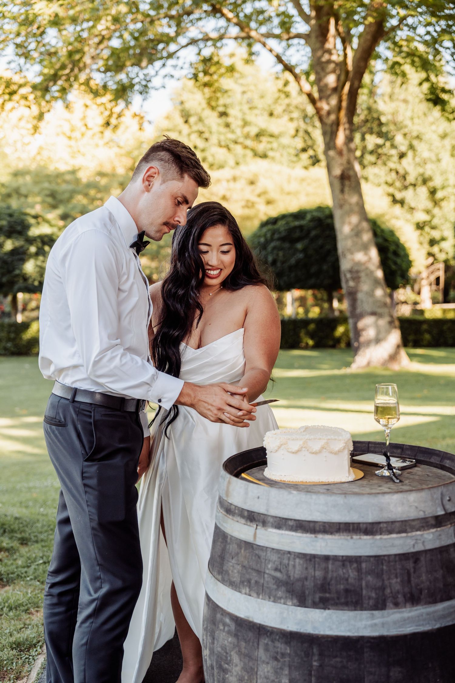 Happy newlyweds embracing beside their wedding cake on a wooden barrel in garden.