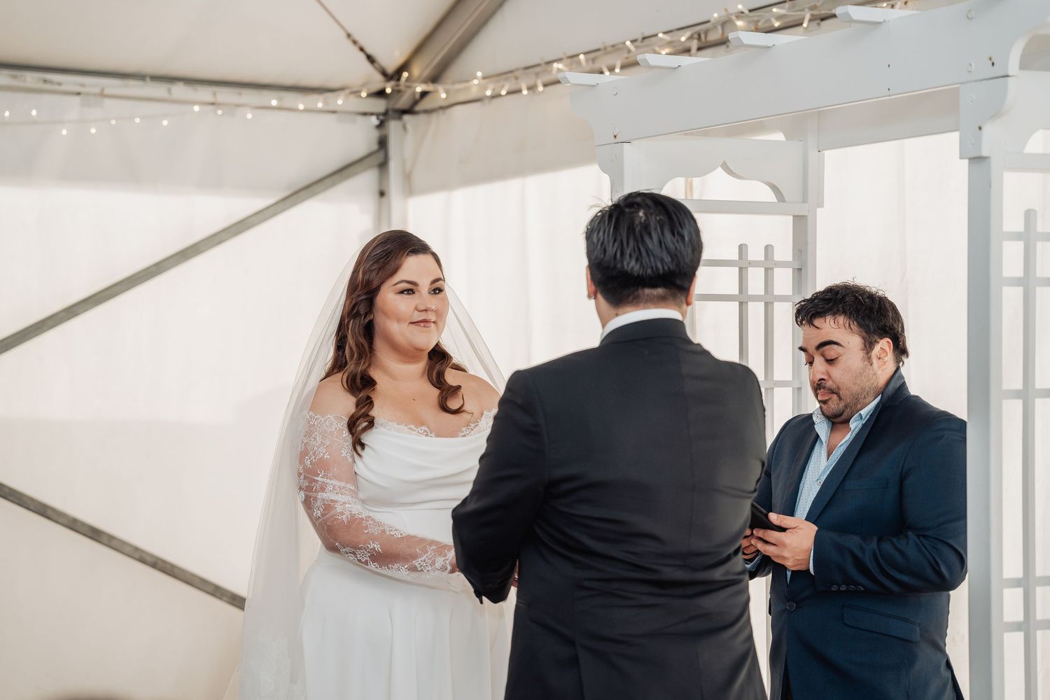 A joyful wedding ceremony takes place inside a white tent with fabric draping and sunlight streaming in.