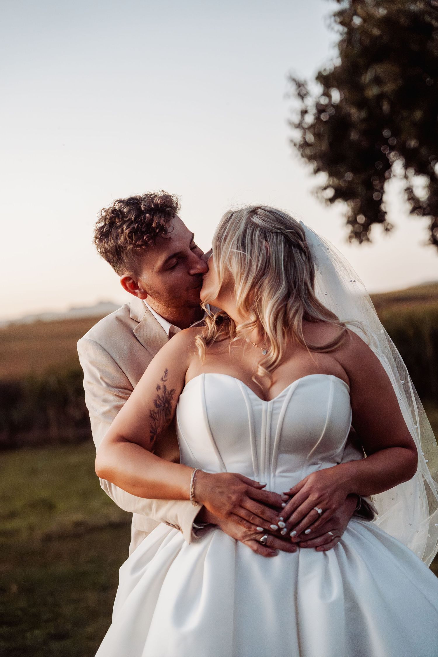 Groom tenderly kissing bride on the cheek at golden hour in a scenic outdoor setting.