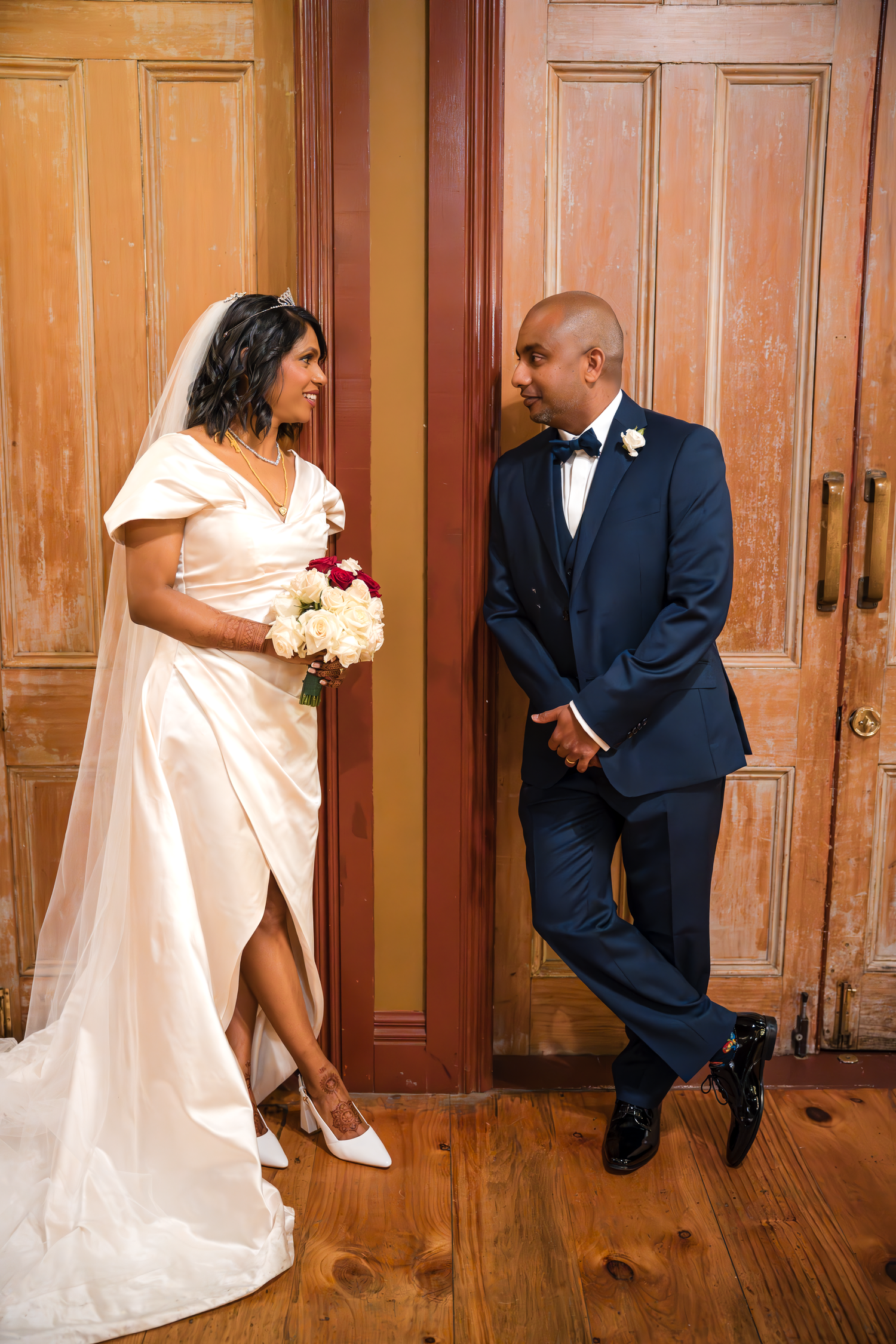 A couple in formal attire pose elegantly against vintage wooden doors.