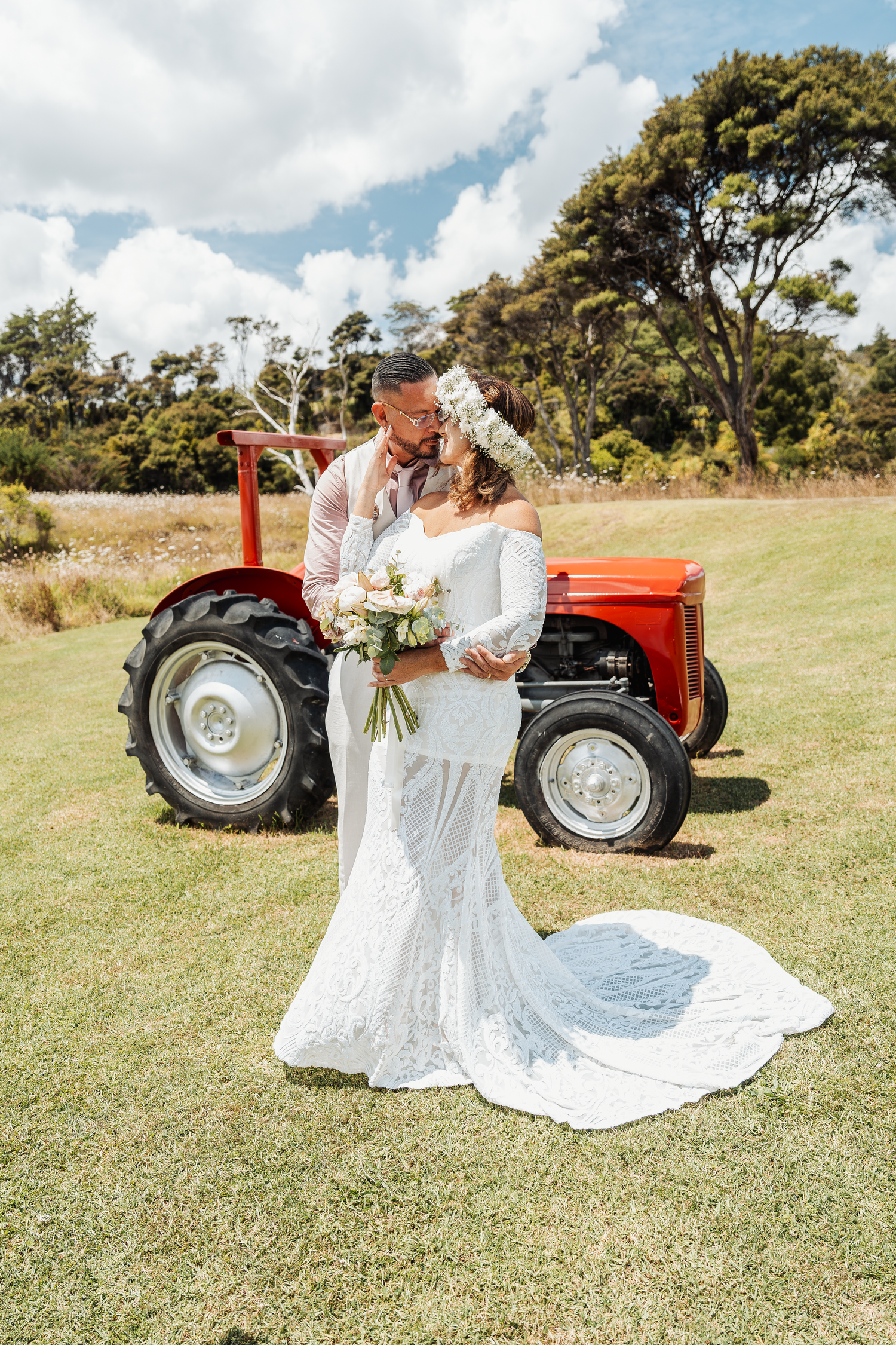 A wedding couple poses with a classic red tractor in a rustic outdoor setting.