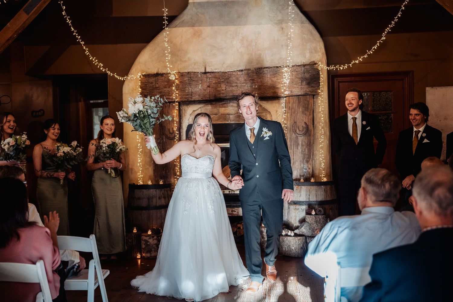 Newlyweds celebrate together during their rustic barn wedding ceremony with guests watching from white chairs.
