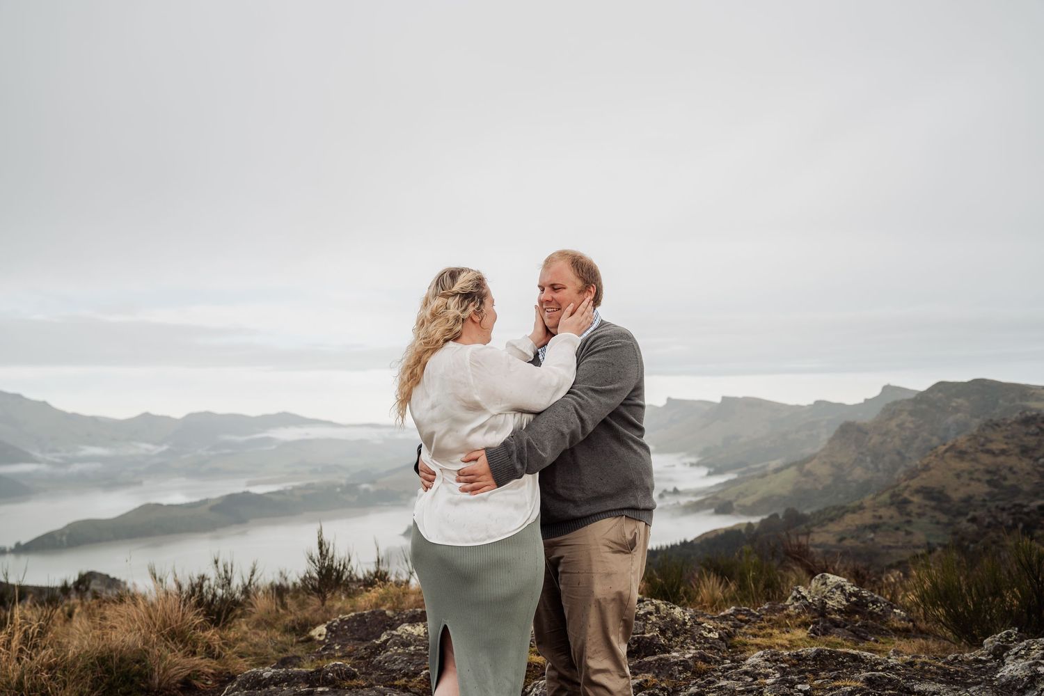 Two people embrace on a mountain summit overlooking a misty valley during a romantic wedding moment.