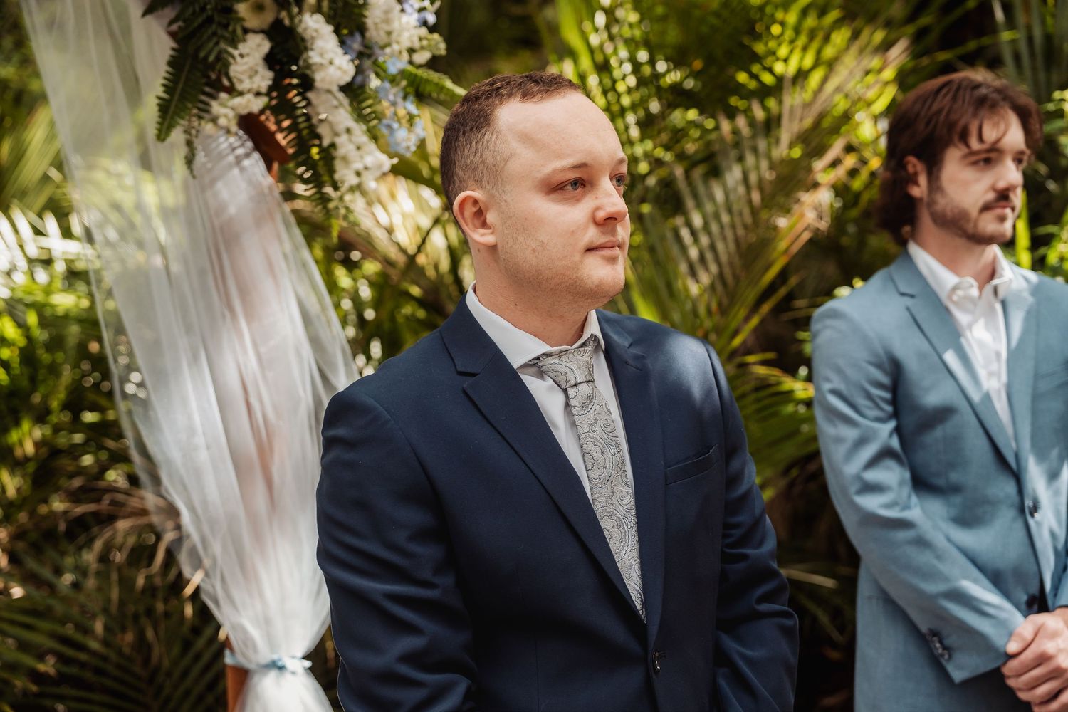 Groomsmen in navy and grey suits standing in formation at an outdoor wedding ceremony.