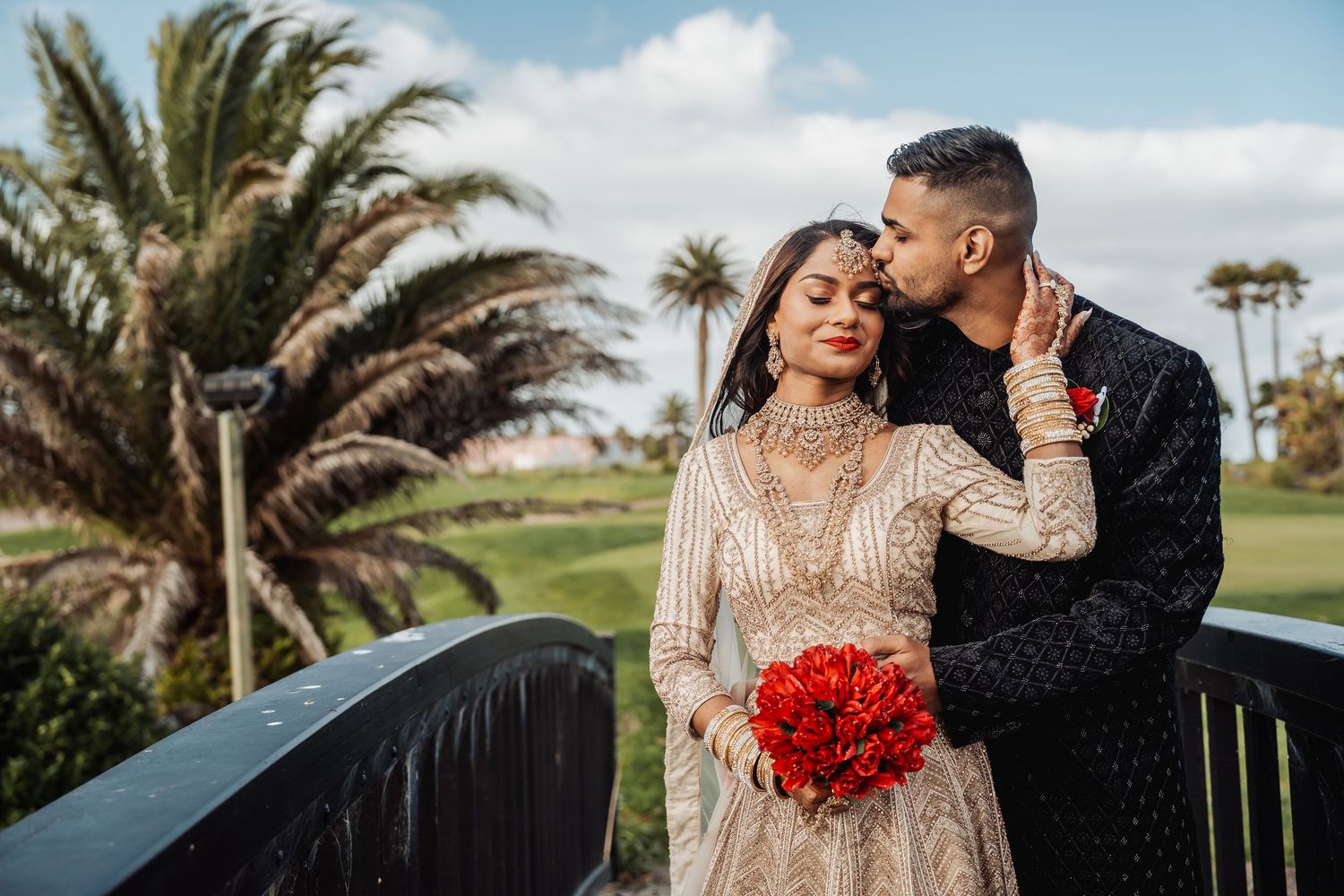 A couple shares intimate moments on an outdoor deck with tropical landscaping and palm trees.