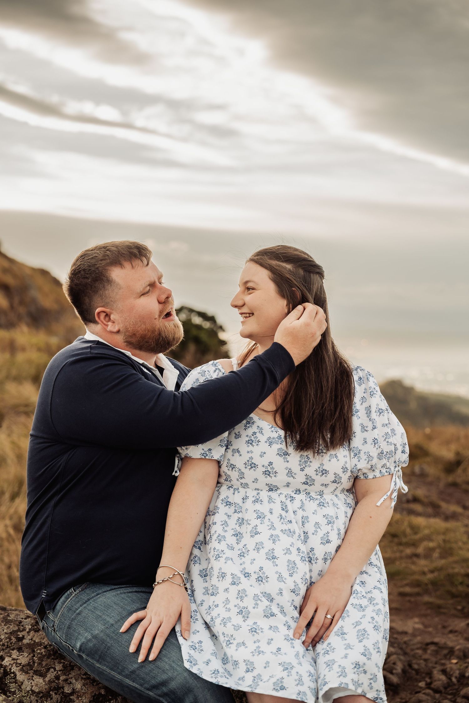 Couple sharing a tender moment on a rocky coastal overlook, man gently touching womans face at sunset.