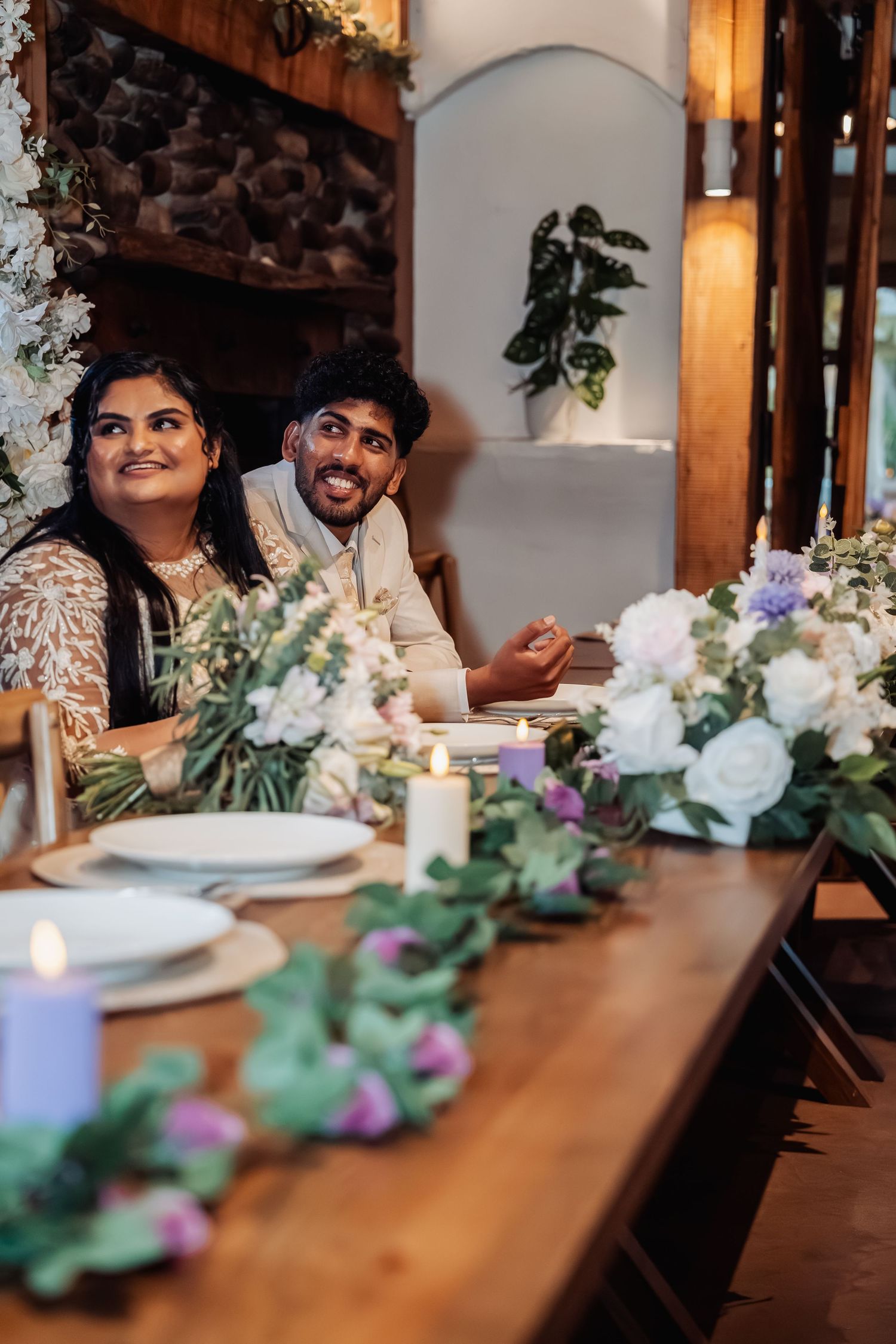 Smiling bride and groom seated at elegantly decorated floral wedding reception table.