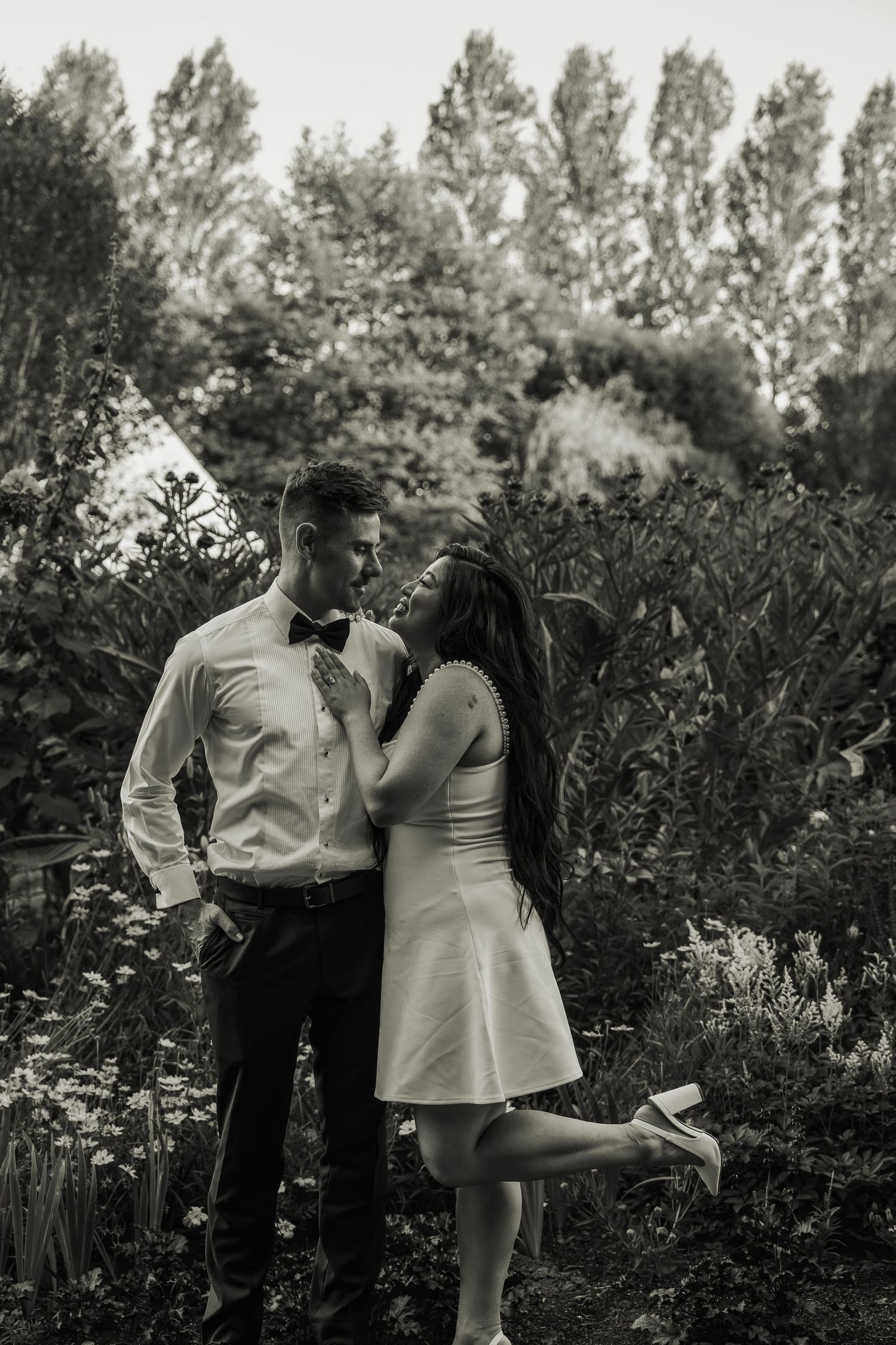 Black and white photo of couple gazing at each other in lush garden.