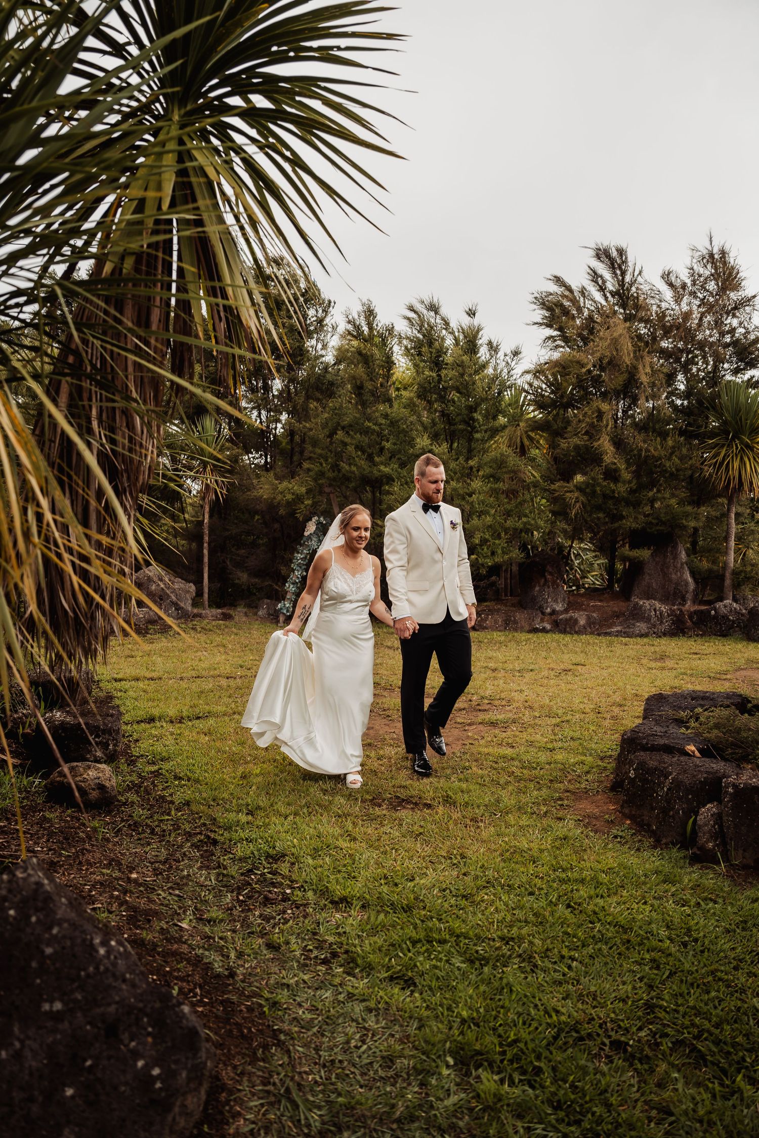 Bride and groom walking hand in hand through tropical garden after wedding ceremony.