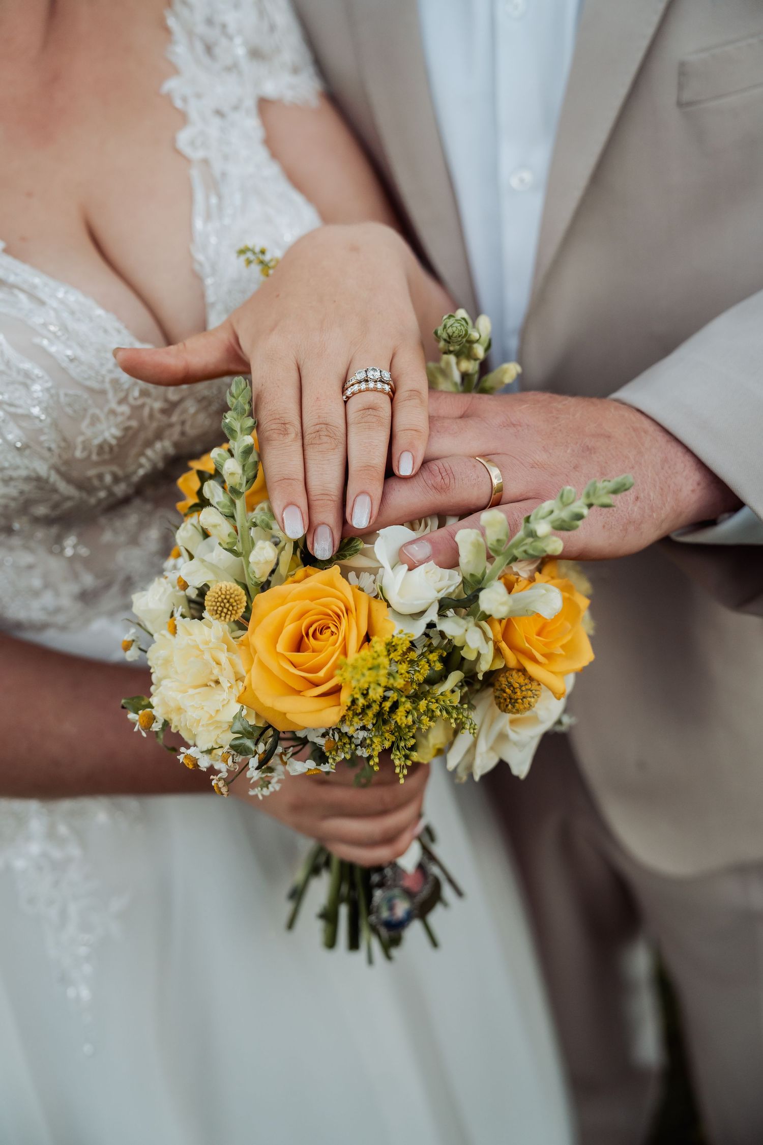 Bride and groom display wedding rings over a bridal bouquet of yellow and white roses.