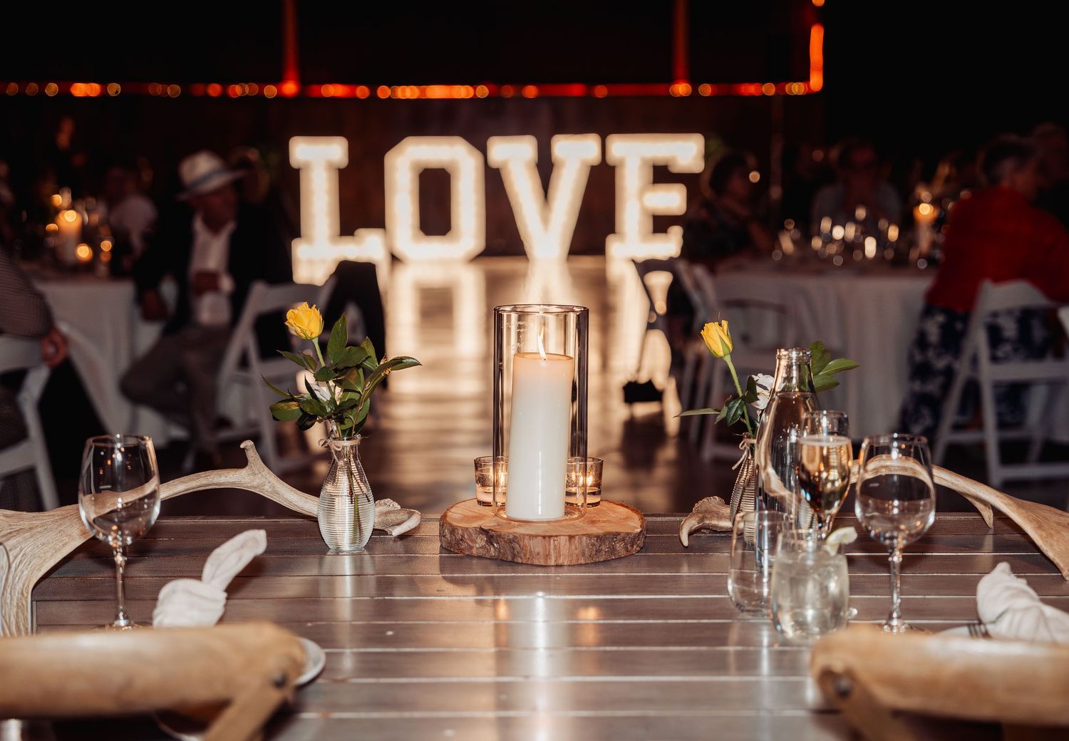 Elegant wedding reception table with LOVE marquee sign, candles, and yellow floral accents.