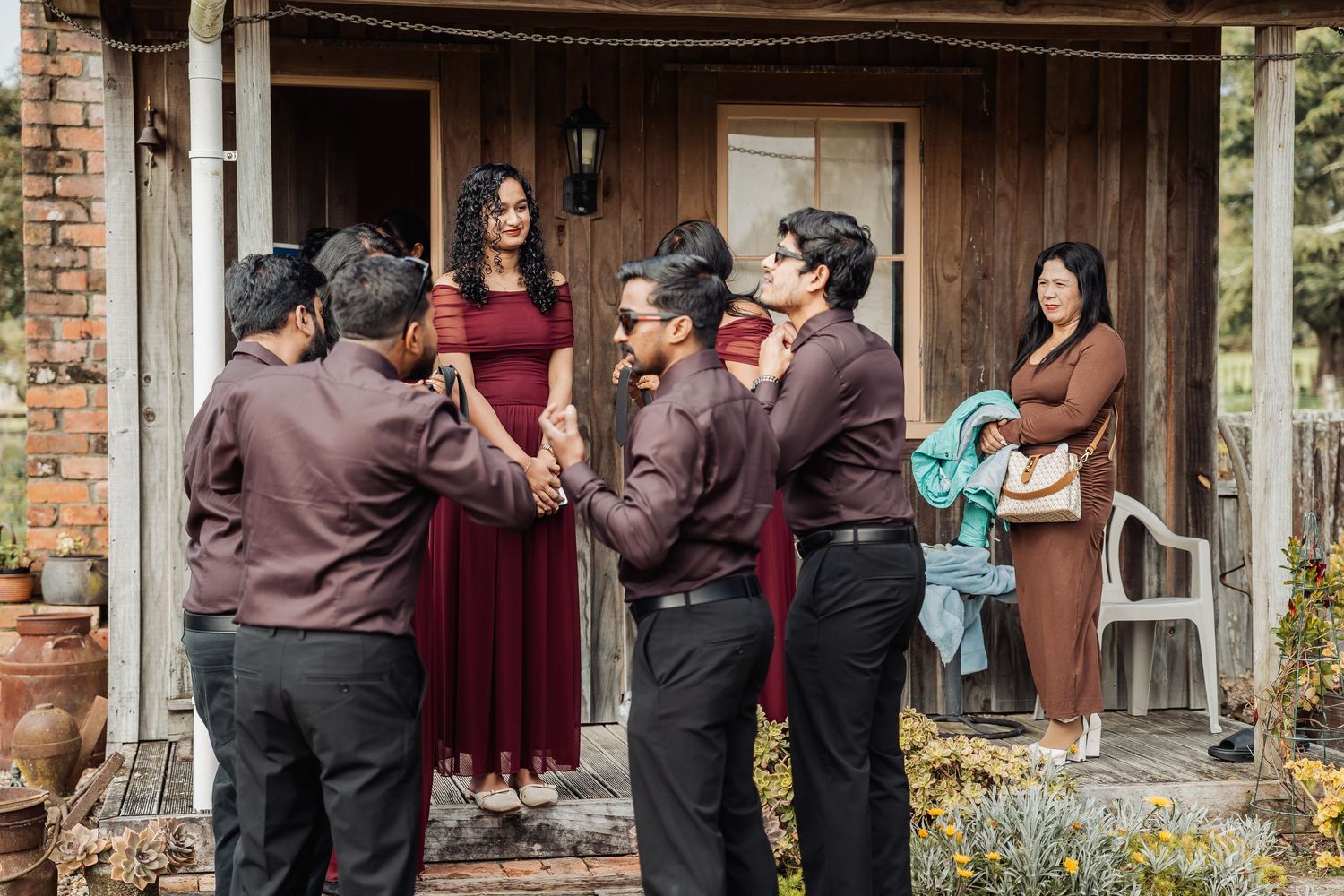 Group of people in maroon and black formal attire gathered outside a rustic wooden building.