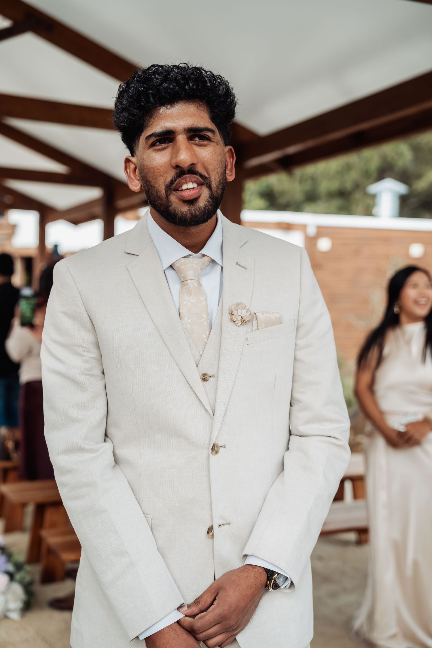 Emotional groom in cream suit awaiting bride at outdoor wedding ceremony altar.
