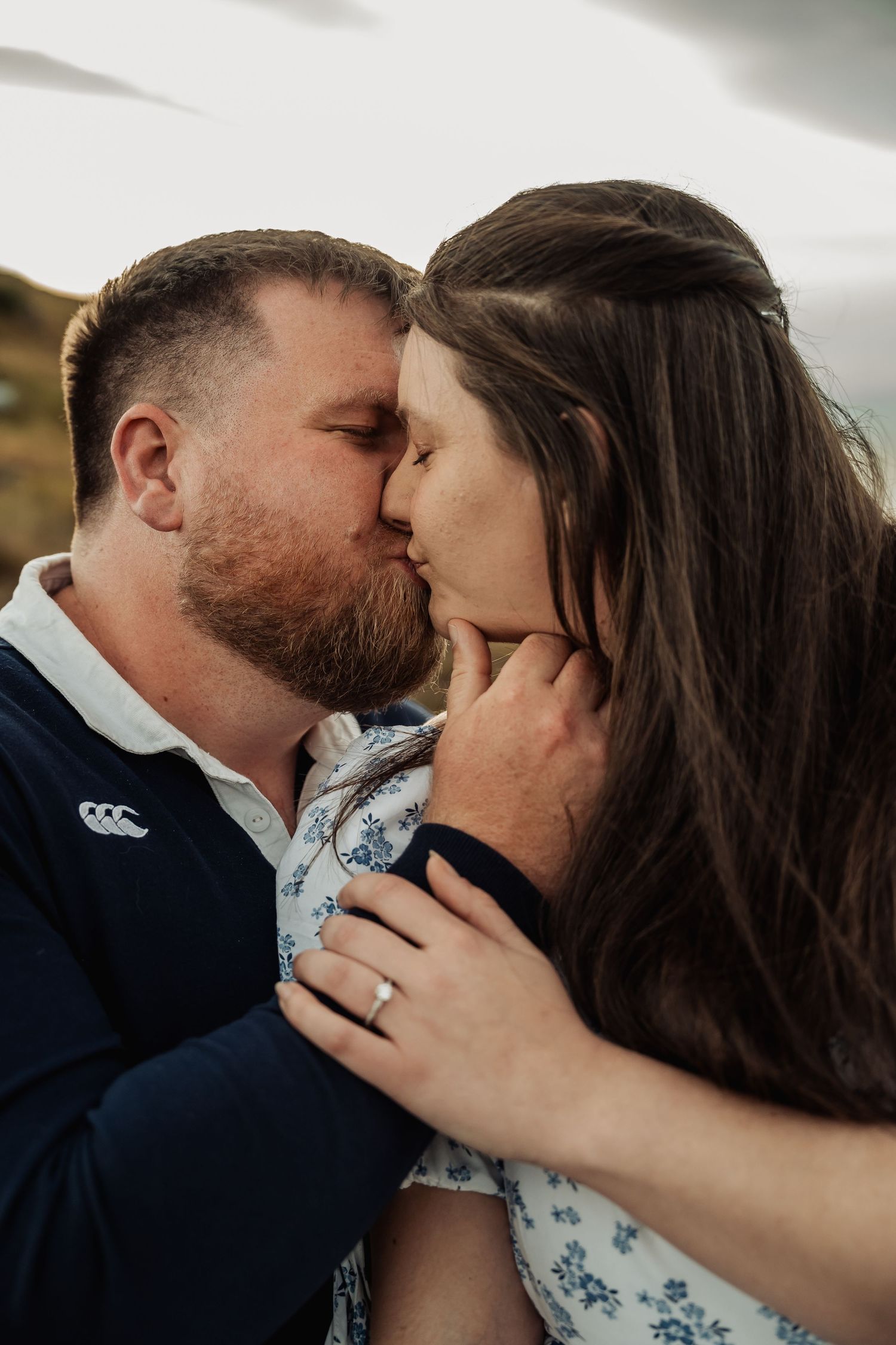 Close-up of couple sharing a romantic kiss outdoors, woman wearing engagement ring on her hand.