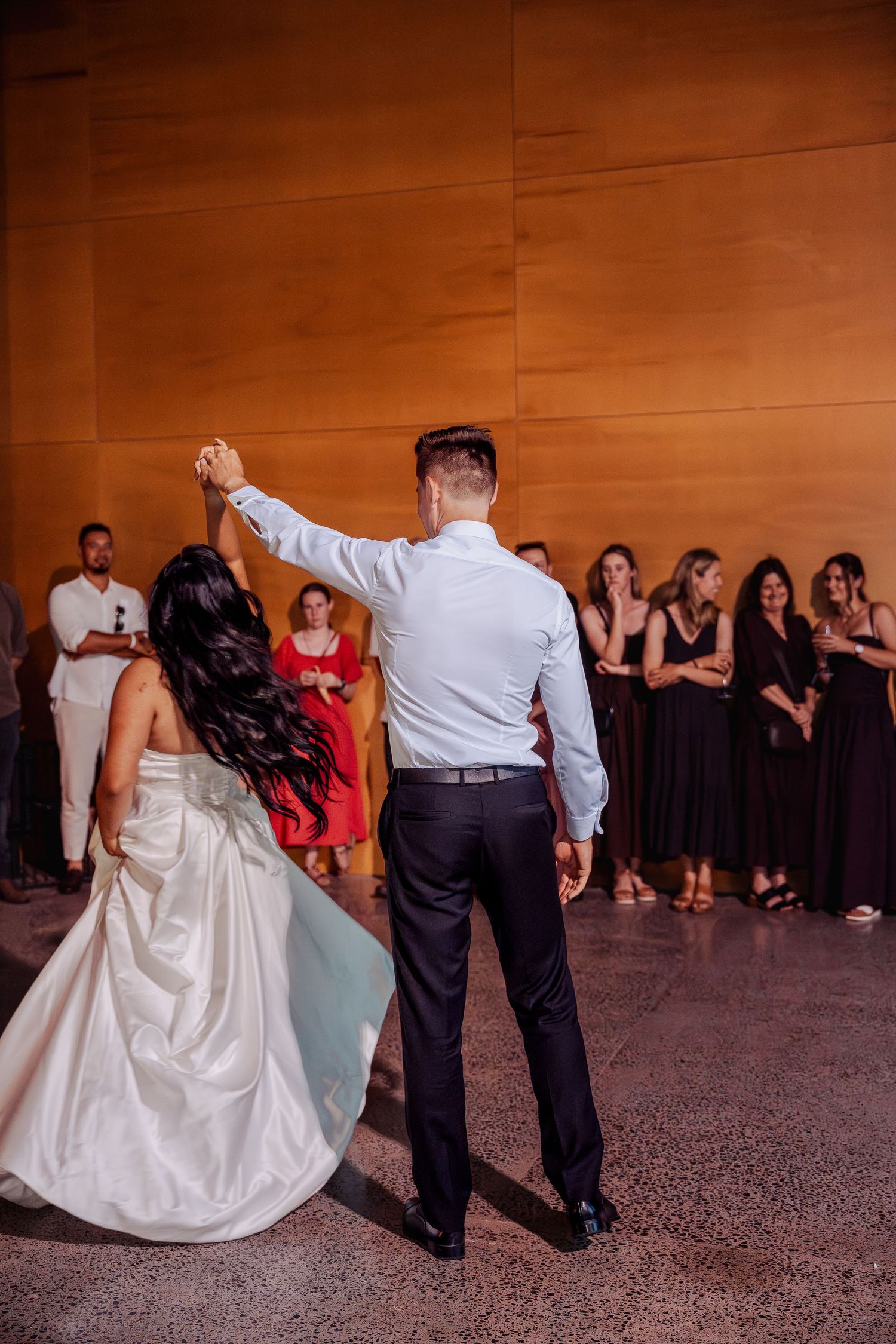 Bride and groom sharing their first dance while guests watch in a warmly lit wedding venue.