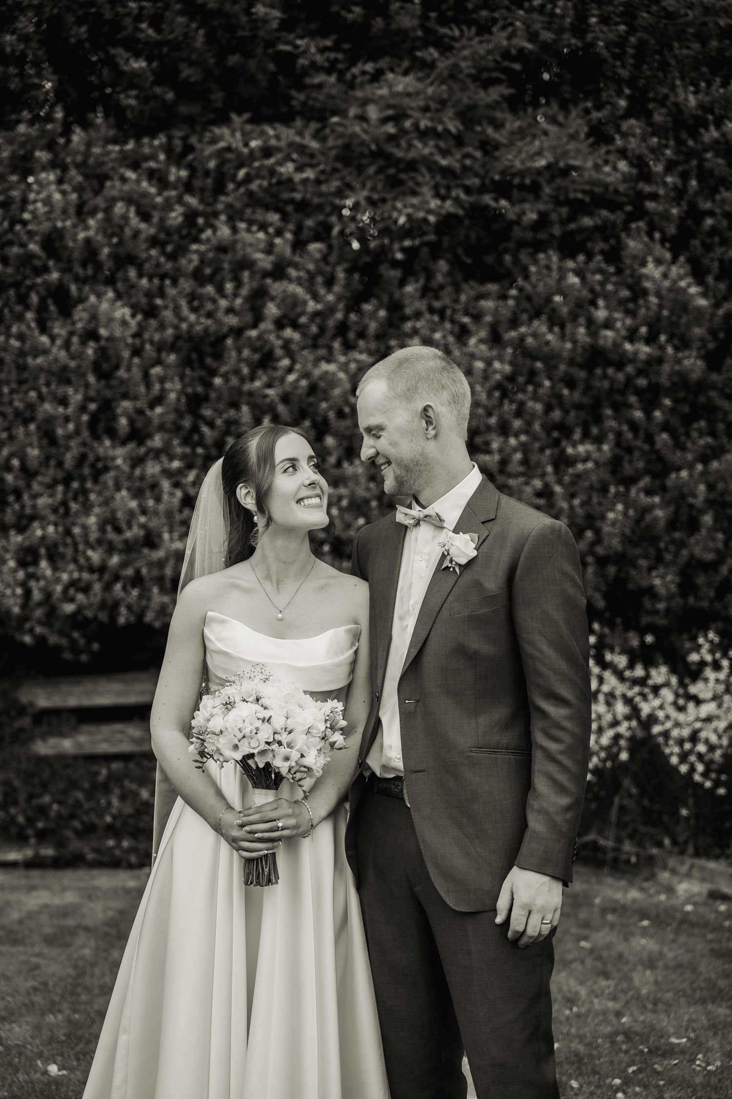 Black and white portrait of bride and groom gazing at each other in lush garden setting.