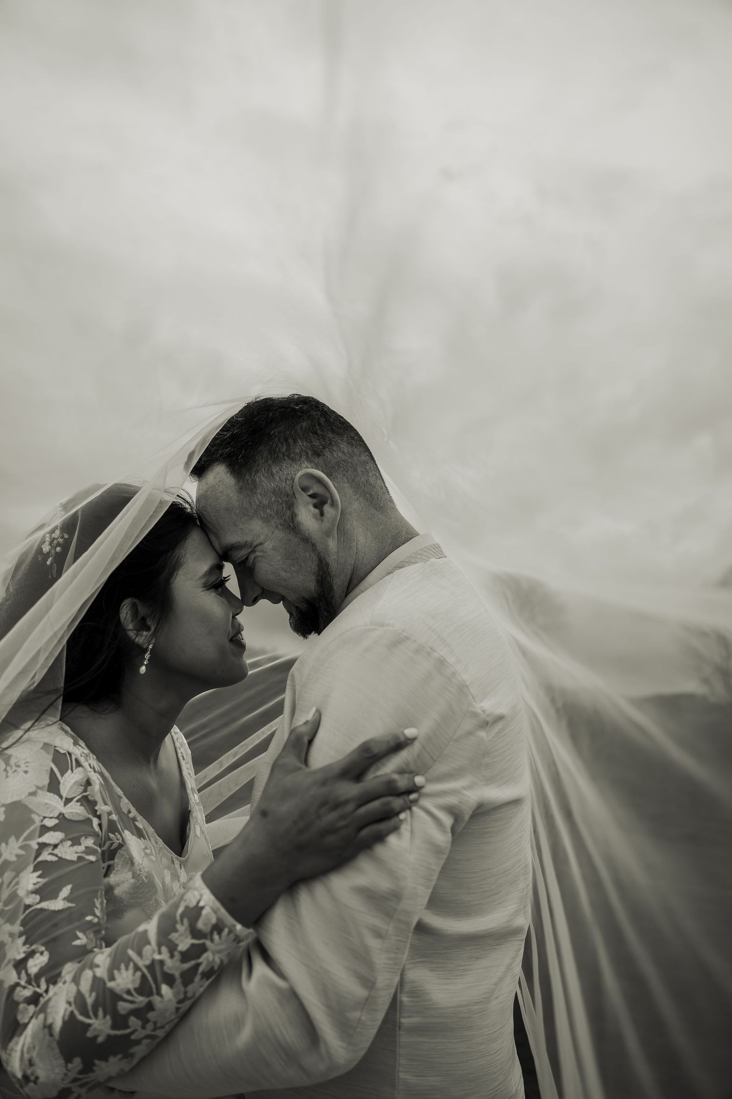 Black and white romantic portrait of a couple sharing an intimate moment under a wedding veil.