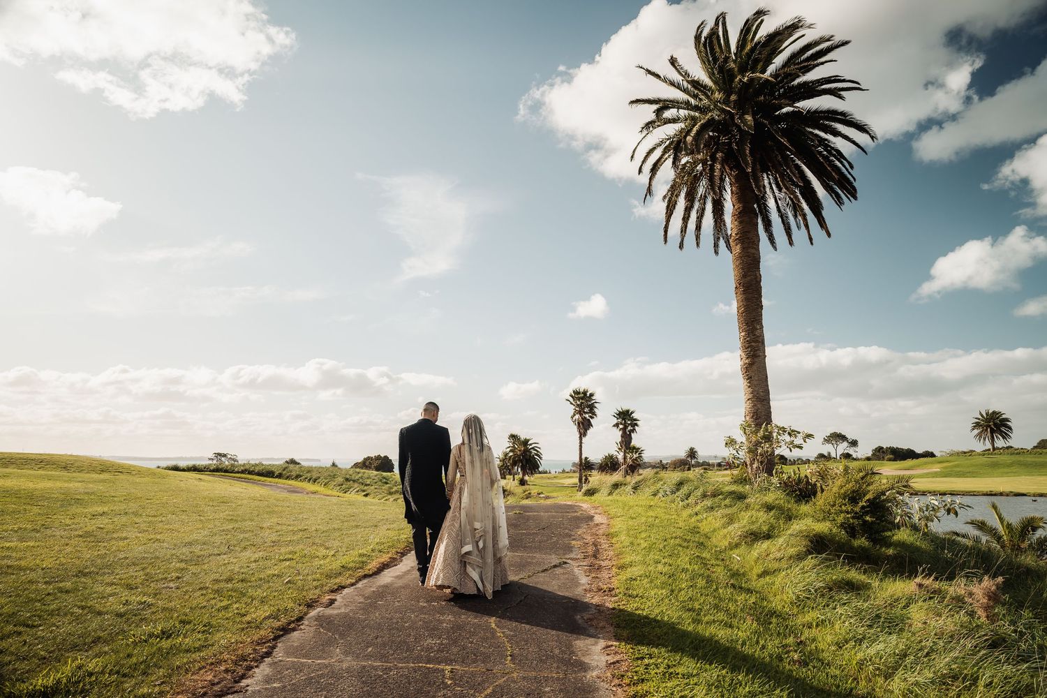 Panoramic wedding photos showing couple walking along coastal path with palm trees and ocean views.