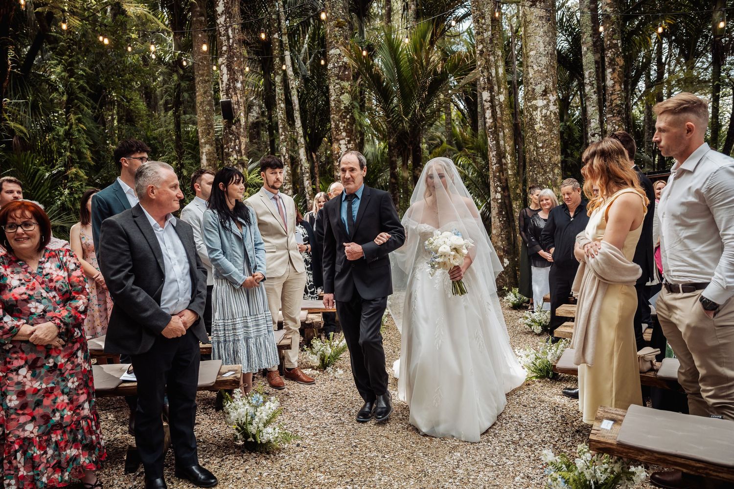 Wedding ceremony guests celebrate in a wooded outdoor setting.