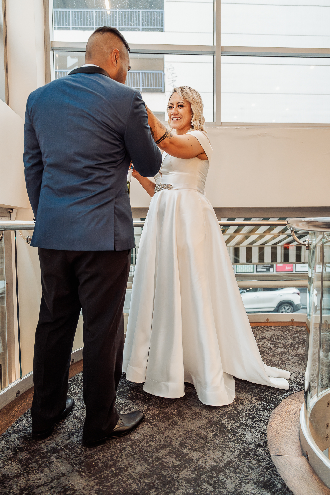Couple in wedding attire shares an intimate moment on modern staircase with glass railings.