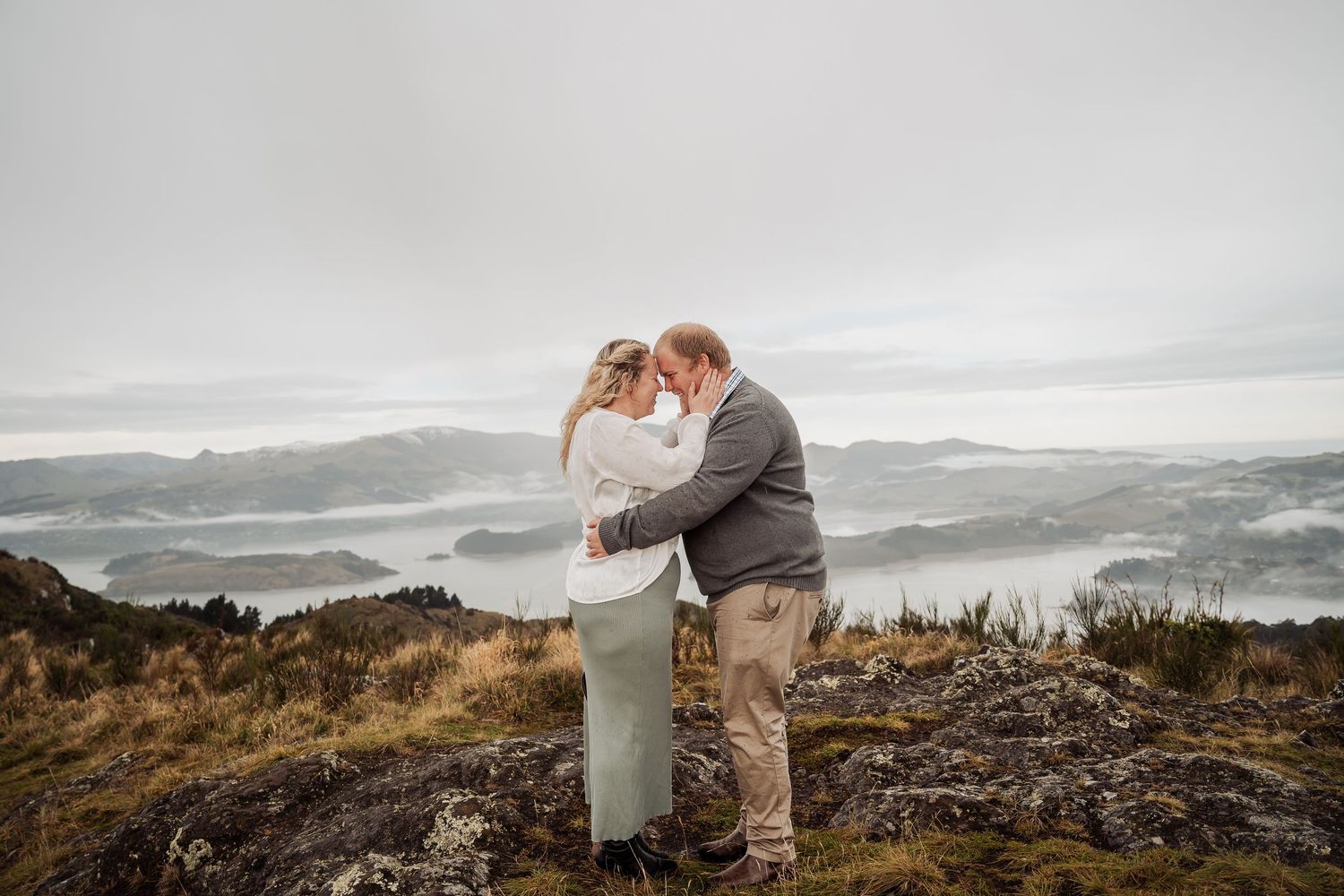 A couple stands on a mountain ridge embracing with a misty landscape background behind them in Oregon.