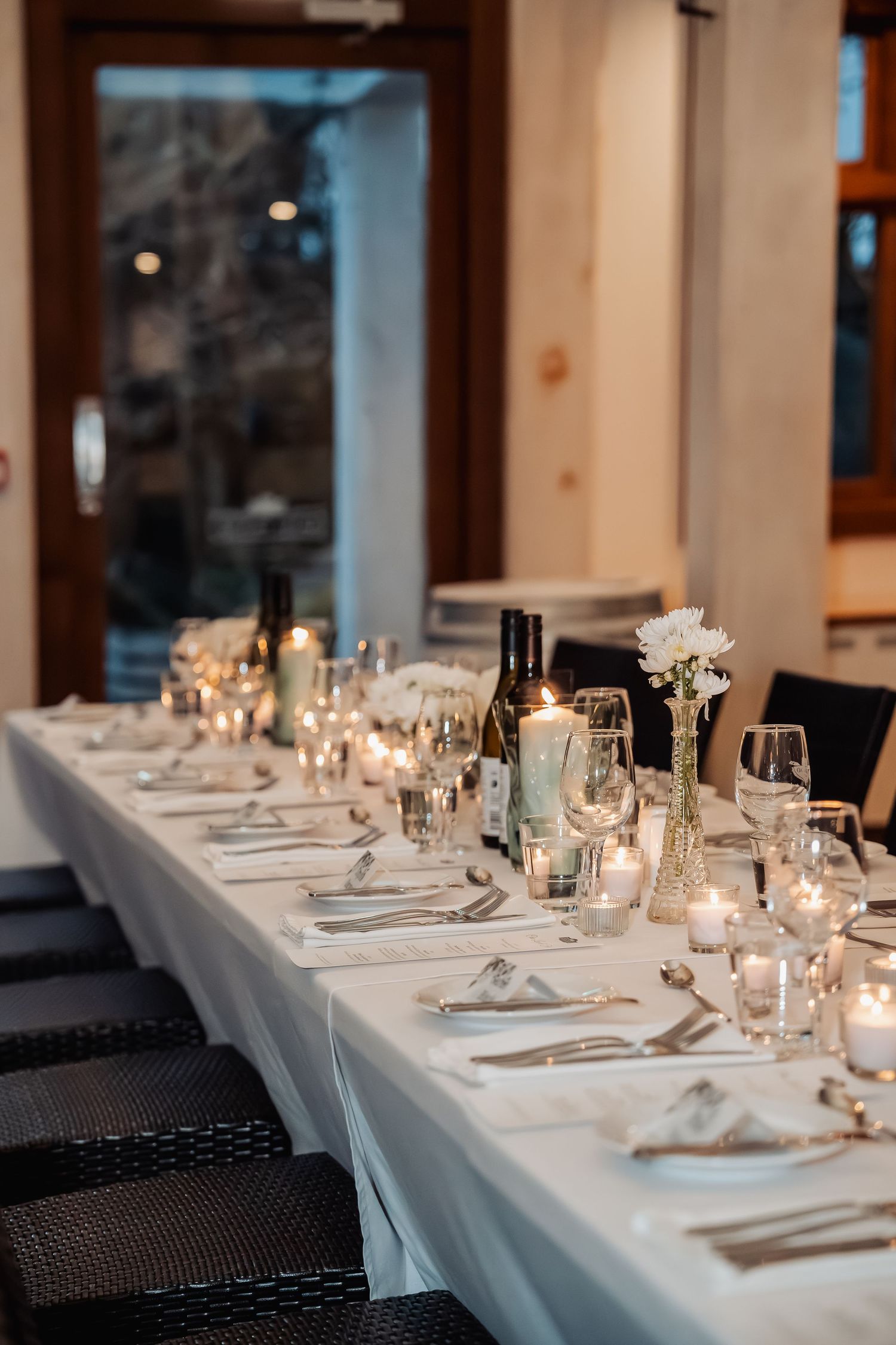 Long elegant table setting with white linens, candlelight and formal place settings at an upscale event venue.