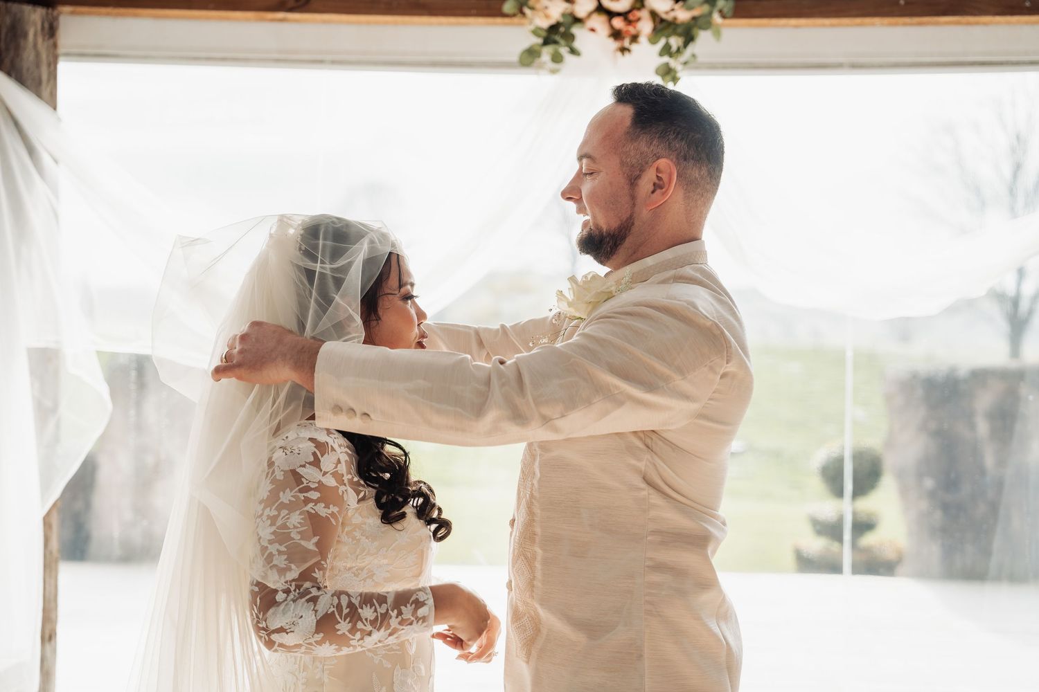 A romantic first dance moment captured under a wooden beam decorated with floral arrangements.