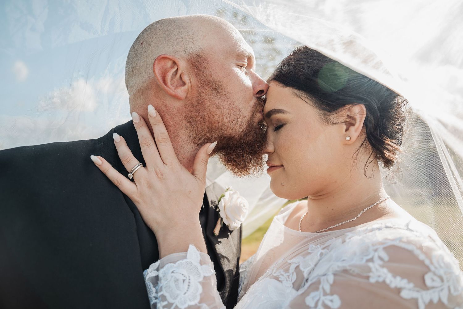 A tender wedding moment captured in sunlight with lace dress details and gentle embrace between newlyweds.
