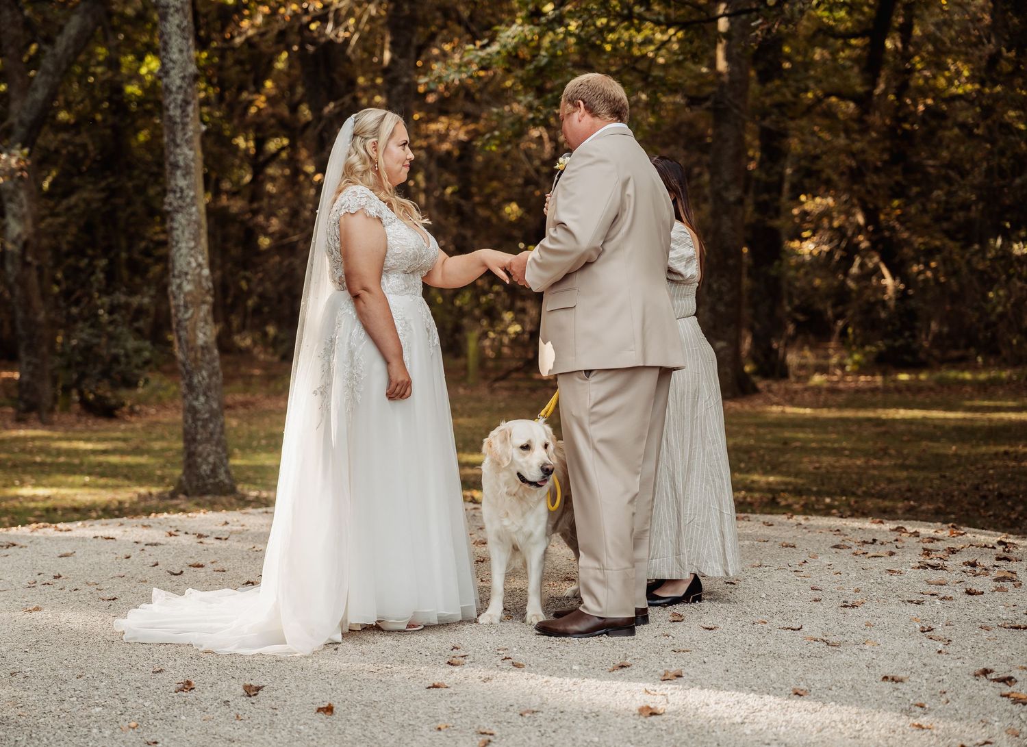 Bride and groom hold hands during intimate outdoor wedding ceremony with white dog standing beside them.