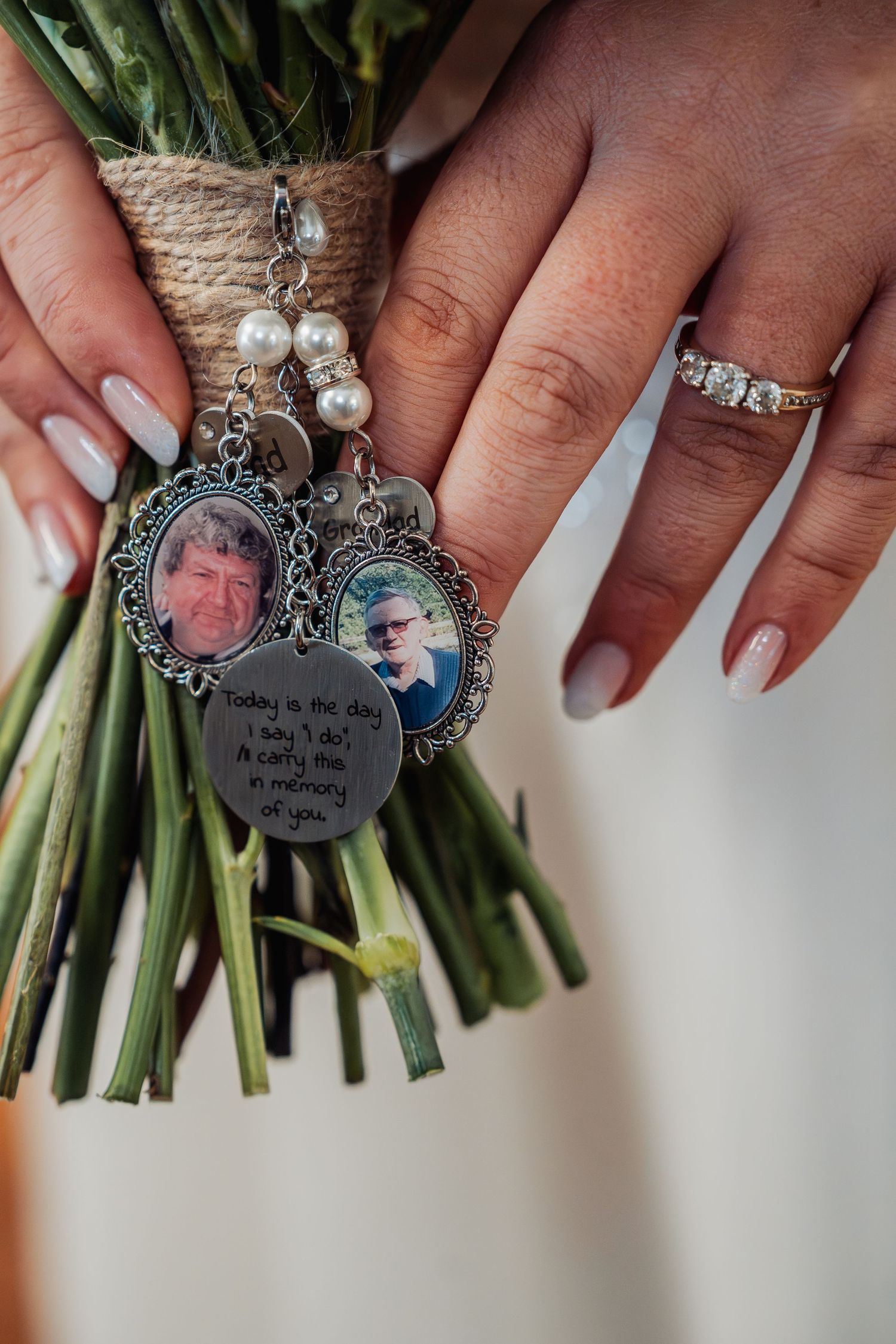Bride holds bouquet with memorial photo charms and pearl accents, wearing diamond ring on wedding day.