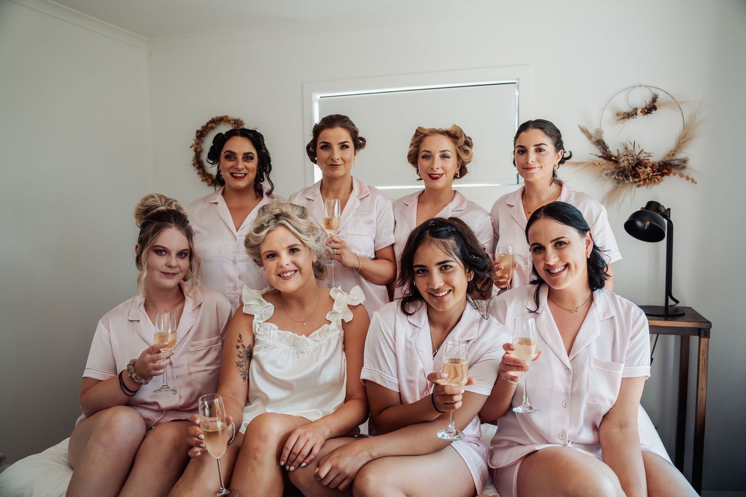 Bride and bridesmaids in matching pink satin pajamas celebrating with champagne glasses before the wedding.