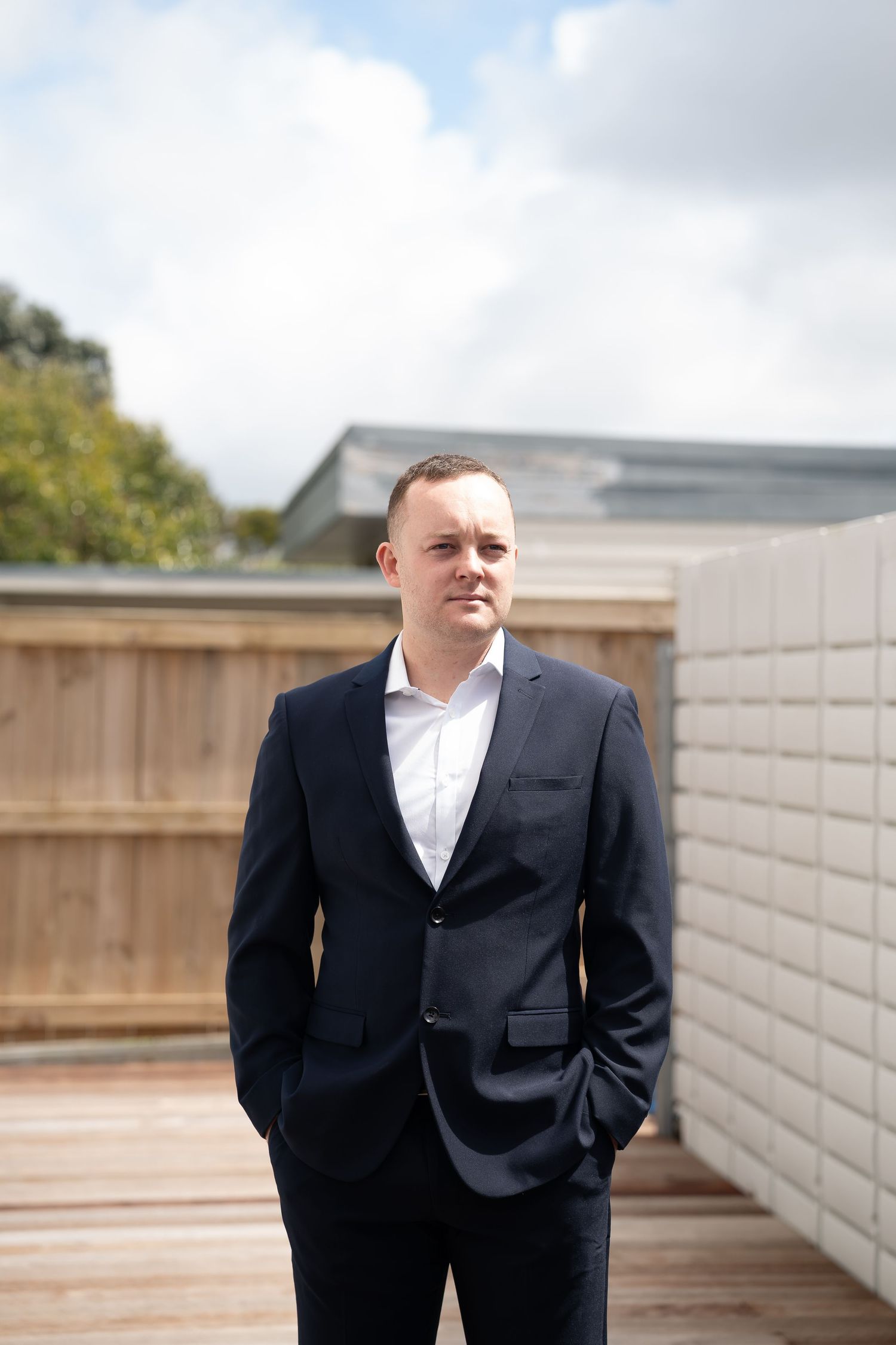 Groom in a black suit and white shirt poses against a modern concrete wall backdrop.