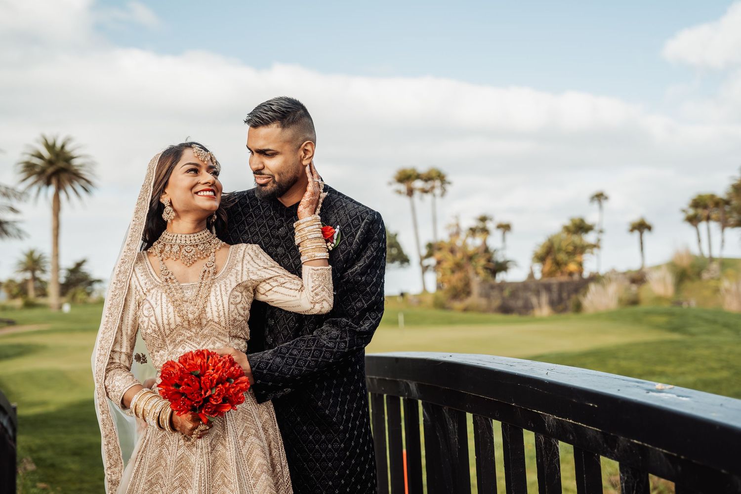 A couple in formal attire shares a romantic moment on a golf course with palm trees in the background.