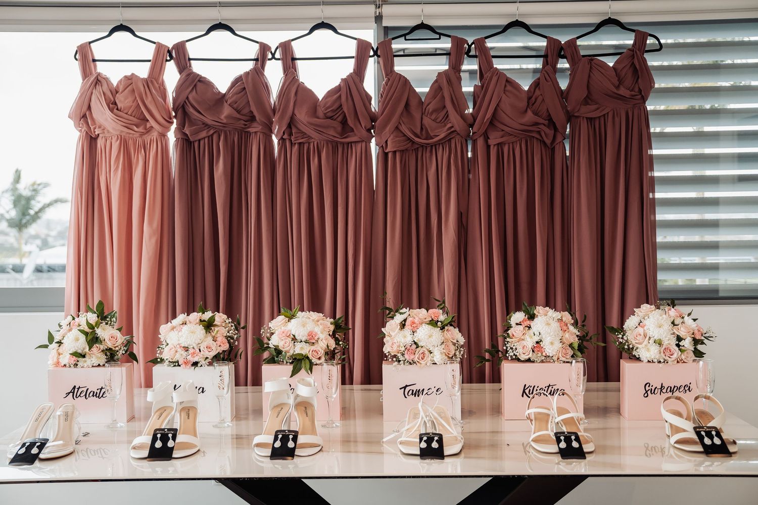 Dusty rose bridesmaid dresses hanging with matching floral bouquets and name cards displayed below.