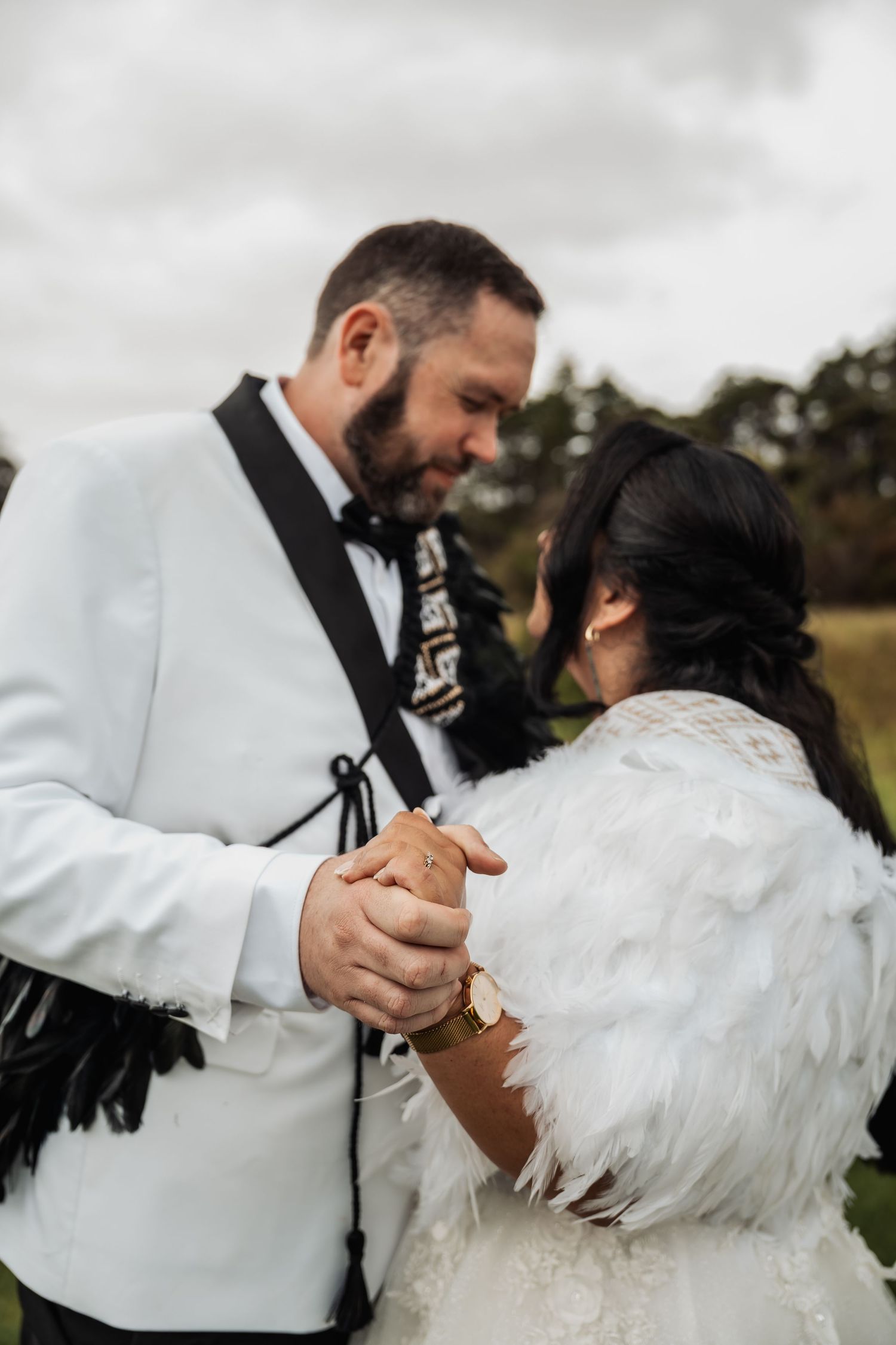 Bride and groom in feathered wedding attire holding hands and sharing intimate moment outdoors.